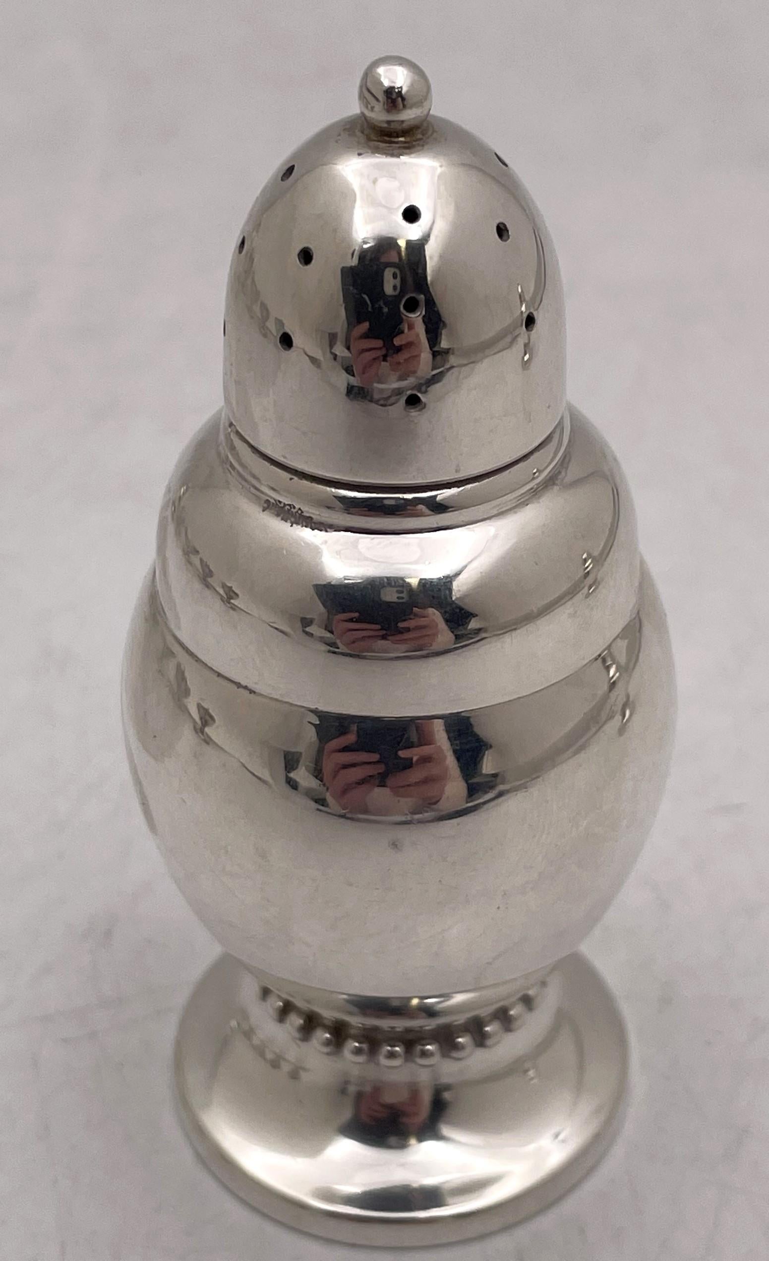 Randahl pair of sterling silver salt and pepper shakers in Arts & Crafts style, one with a gilt top, with beaded motifs at the base. They measure 3 1/2'' in height by 1 2/3'' in diameter, weigh 4 troy ounces, and bear hallmarks as shown. 

Along