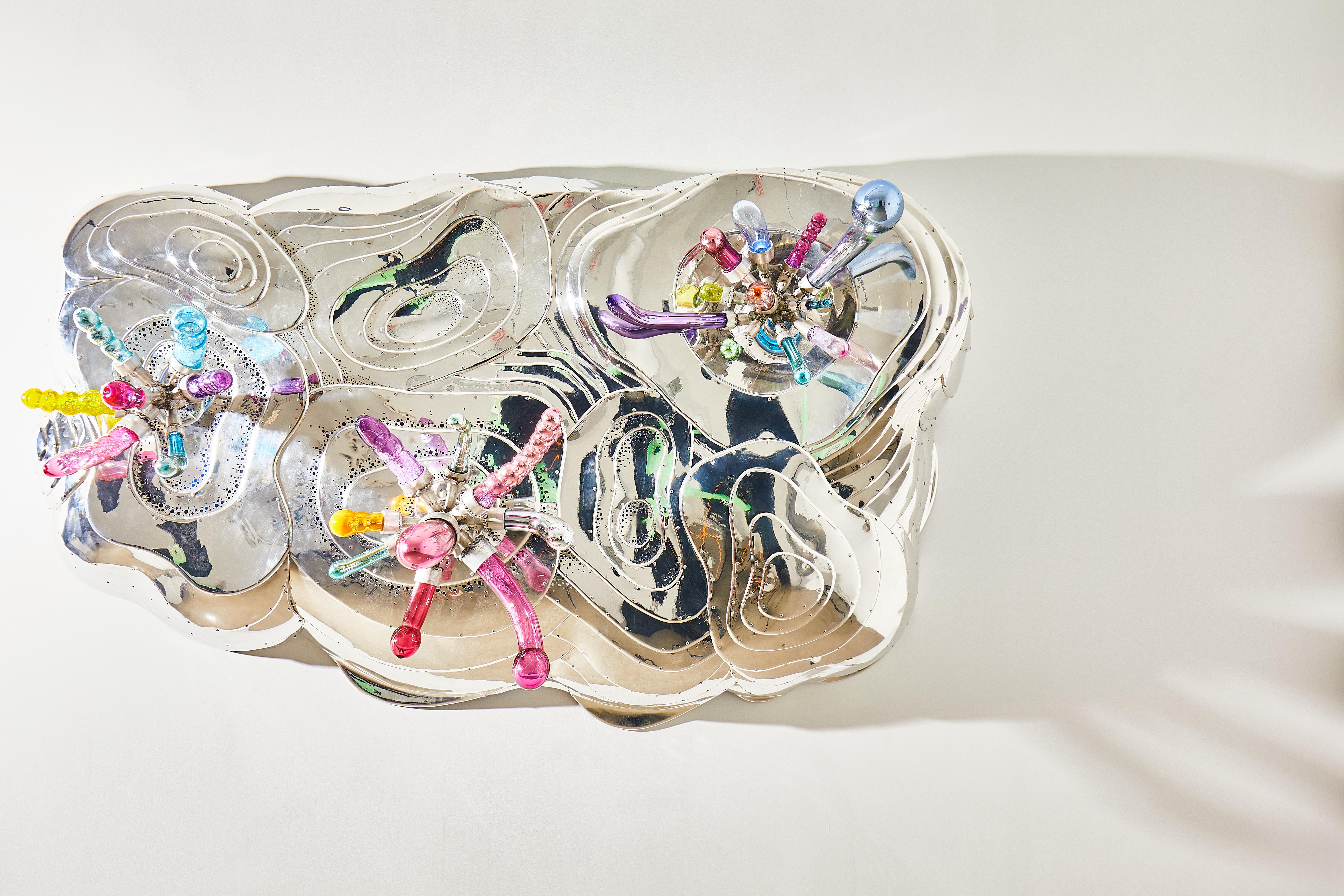 Randy Polumbo
Nebula Lucidum, 2022 
Dimensions: 43” H x 51” W x18” D
Cast glass, stainless steel, video composition, LED’s

Undulating polychrome light weeps from hundreds of tiny backlit perforations, as hand-blown, mercury-mirrored glass
