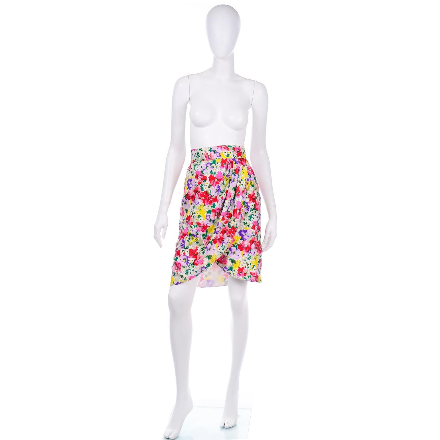 This is a vintage Raoul Arango colorful floral wrap style skirt in a multi colored silk.  The beautiful print is in shades of purple, pink, red, green, white, yellow, and lavender with black outlining. The hem of the skirt is rounded and is slightly