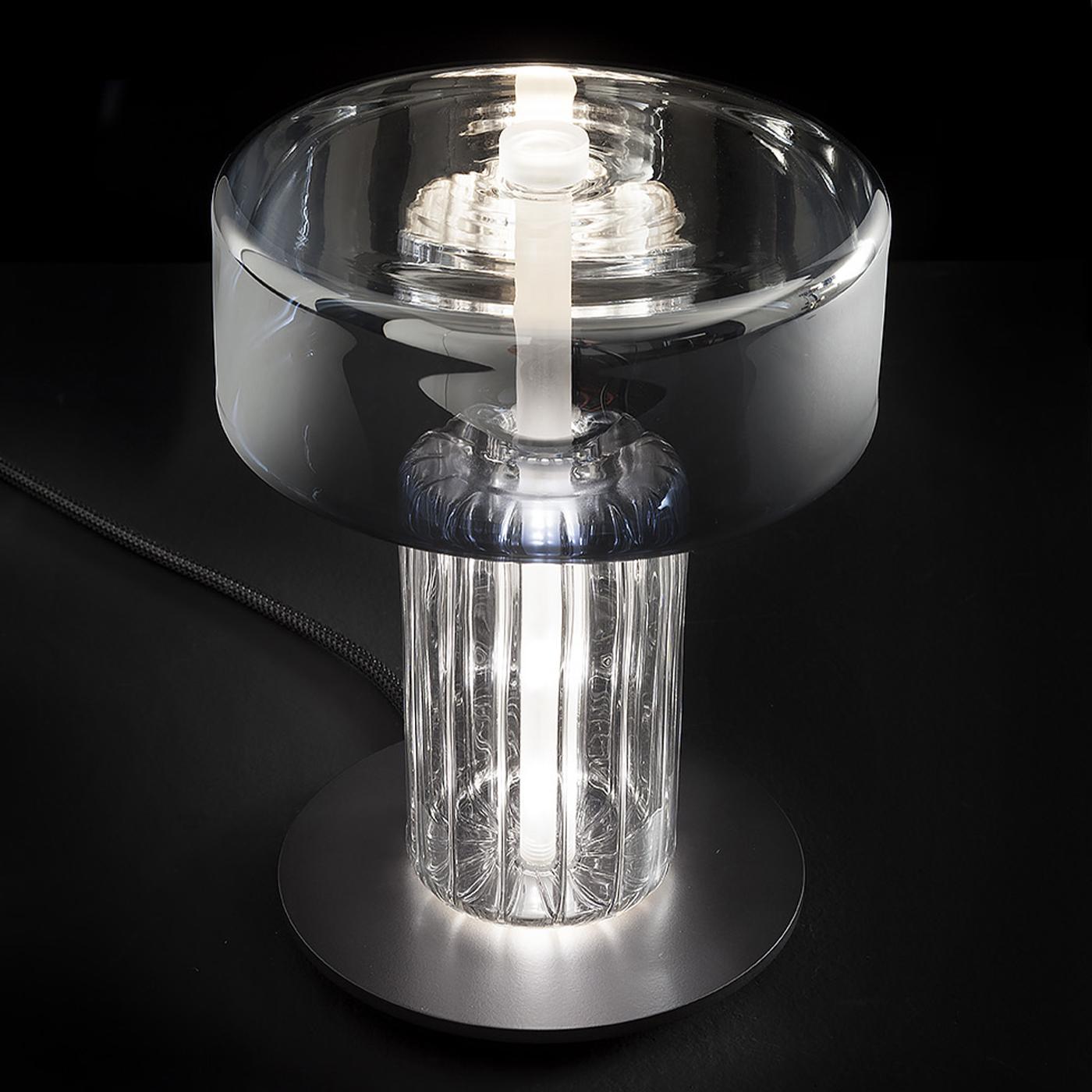 Think about primordial statues, but it is light glass indeed. A table lamp with gold and steel finishes and mirrored effects mixed with a strong design. A triumph of solidity with the touch of lightness of hand blown glass.