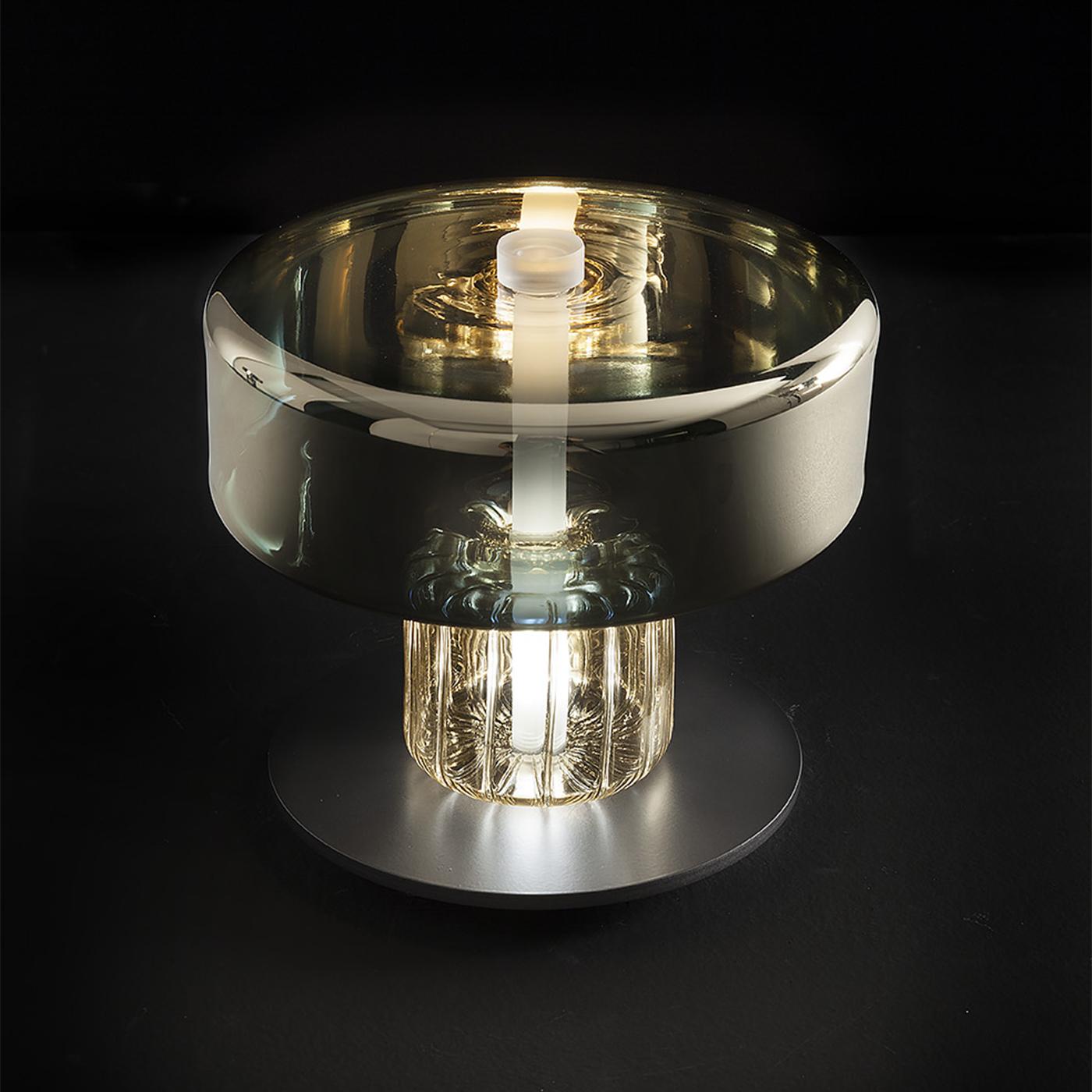 Think about primordial statues, but it is light glass indeed. A table lamp with gold and steel finishes and mirrored effects mixed with a strong design. A triumph of solidity with the touch of lightness of hand-blown glass.