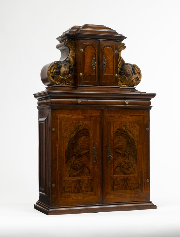 A small architectural table cabinet, veneered in walnut and mulberry, the centre doors enclosing an arrangement of nine various sized drawers with bone knobs, behind a central door a compartment and further three drawers. The cabinet is set with a