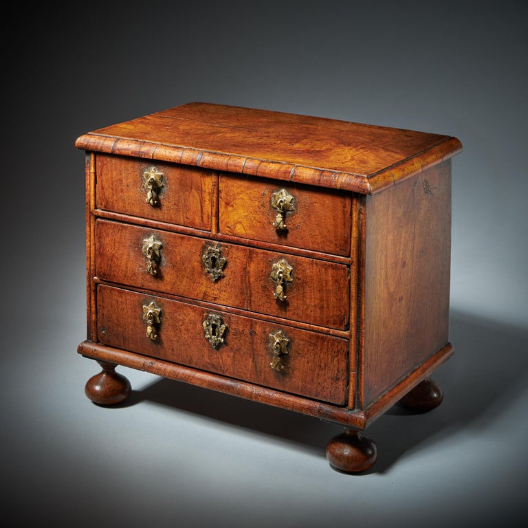 A fine miniature William and Mary 17th century diminutive walnut chest.
From the reign of King William & Queen Mary (1688-1702), England.

The cross-grain moulded top sits above two short and two long walnut veneered oak-lined drawers, each