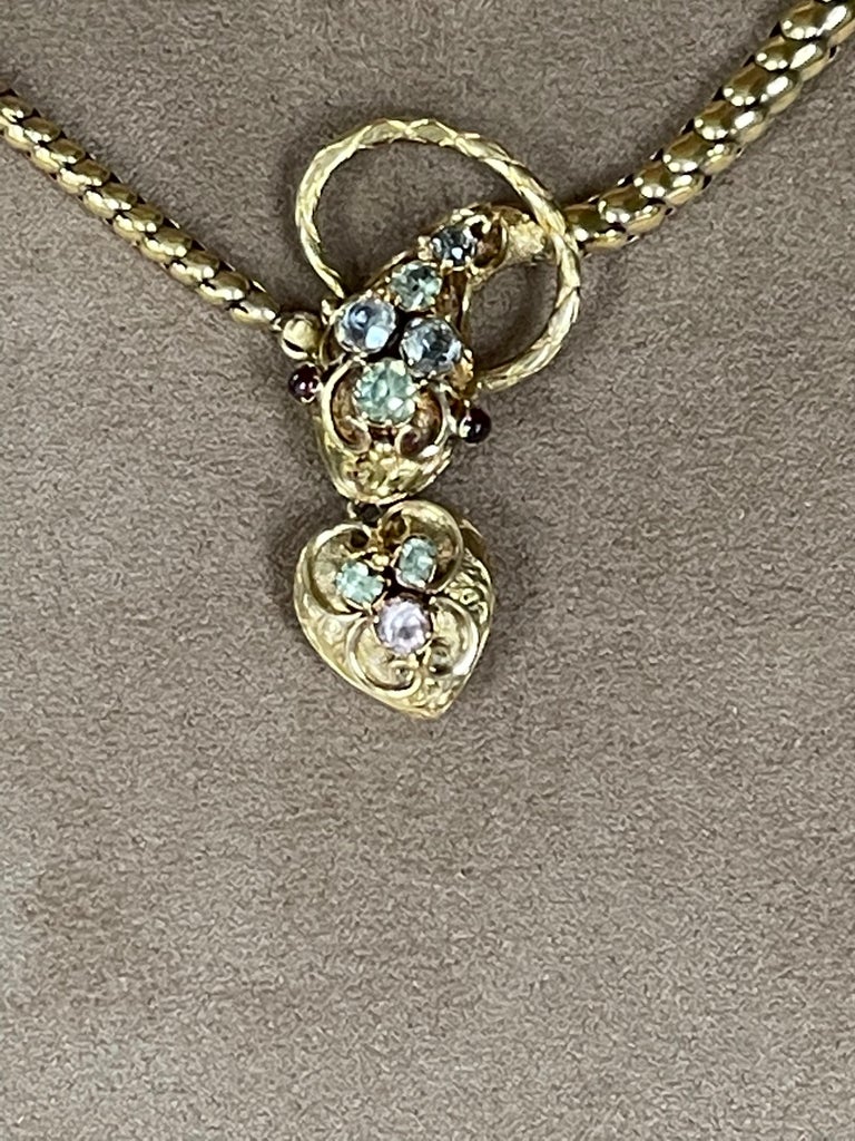 A rare antique Victorian Snake Necklace with a Heart Locket Pendant hanging from its mouth.  The snake necklace dating to circa 1840.  The snake head and the suspending heart are set with colored stones. The eyes are round cabochon Garnets of a