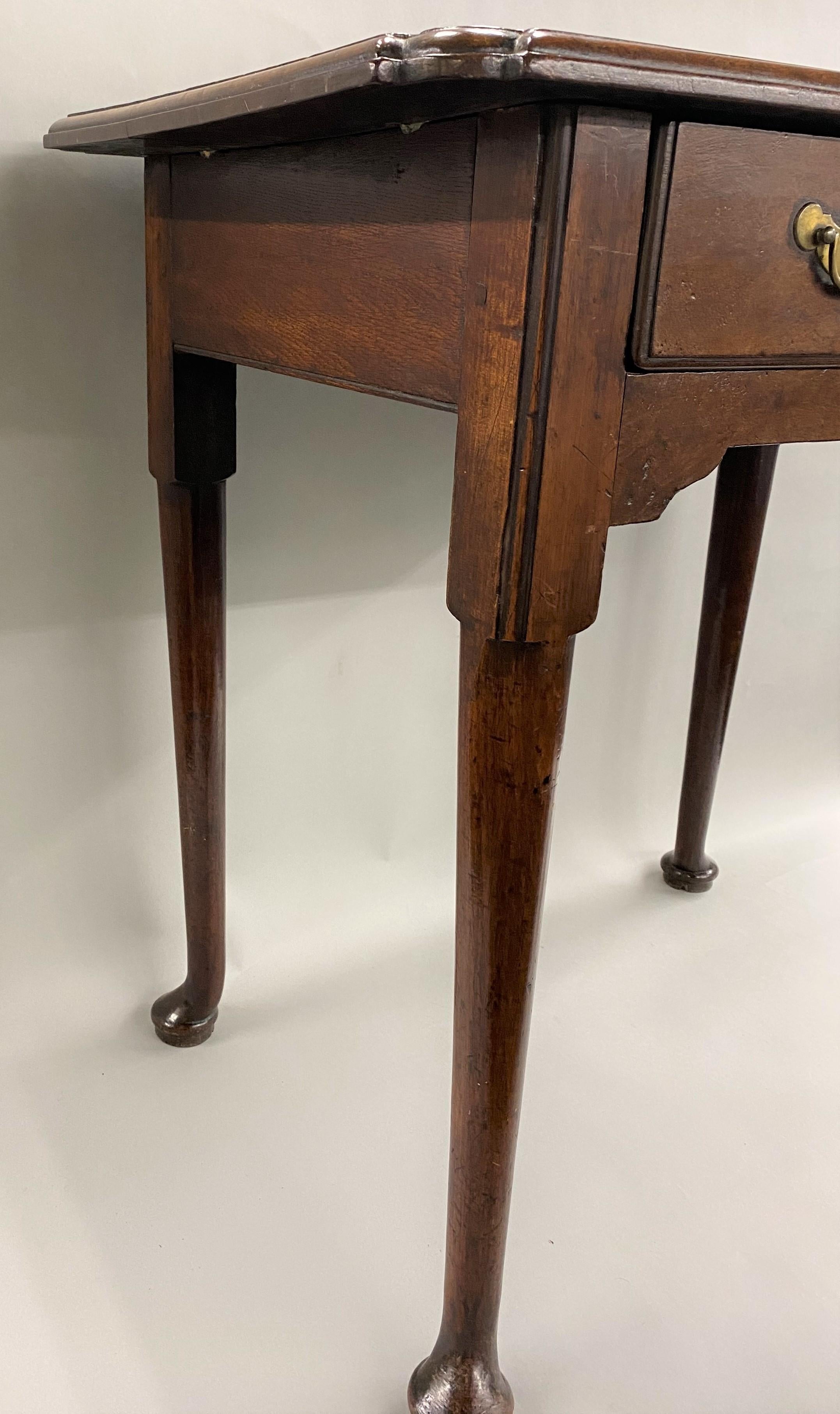 A rare example of an 18th century English rectangular one-drawer table in walnut, its top with a molded edge and pinched corners surmounting a case with single dovetailed frieze drawer over an apron with a small carved center drop, supported by four