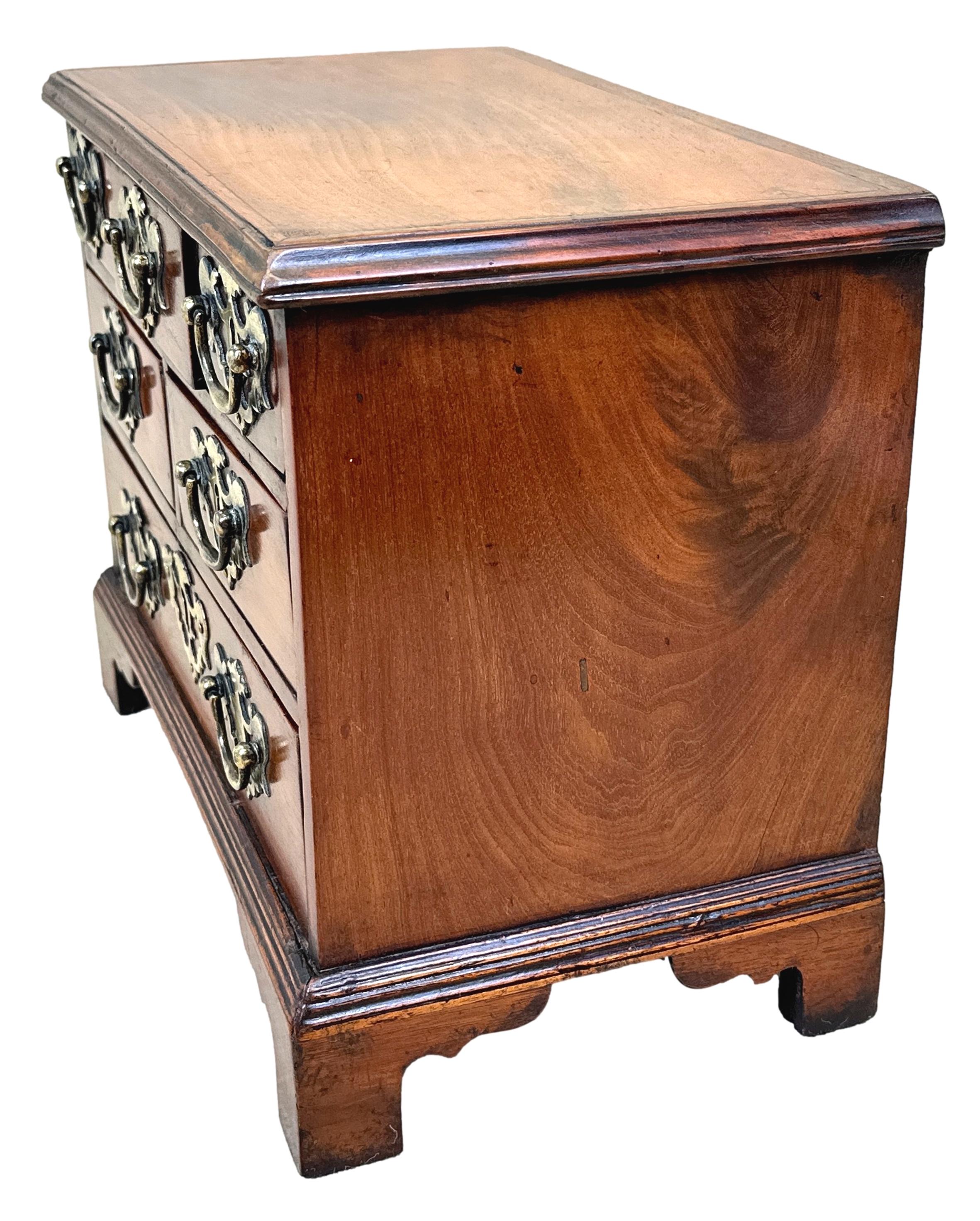A Delightful And Charming 18th Century Mahogany, George II Period, Miniature Chest Having Superbly Figured Top, Over Unusual Arrangement Of Drawers, Retaining Incredible Original Brass Open Plate Handles, Raised On Original Bracket Feet, Retaining