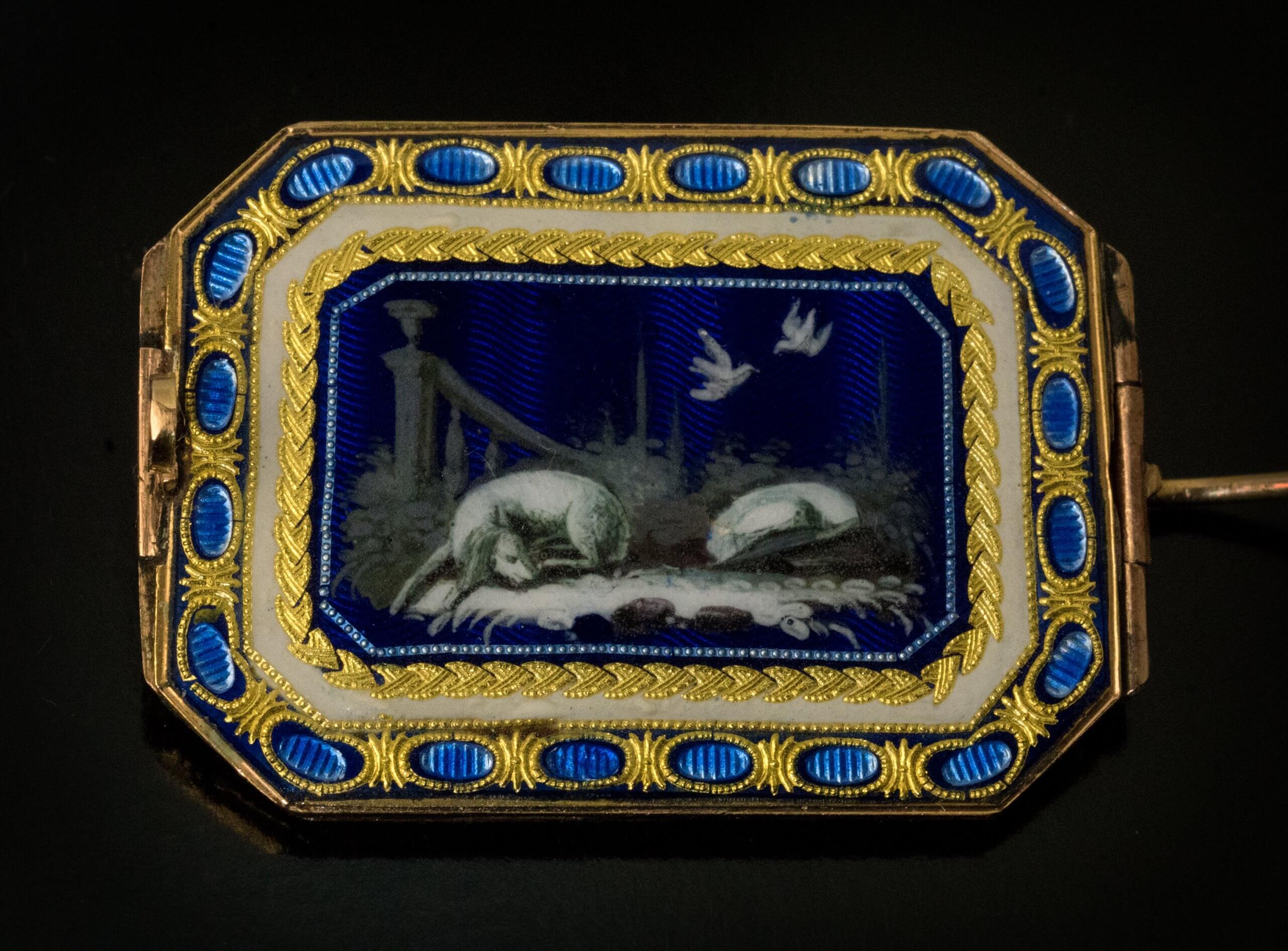 An 18th century enamel on gold brooch embellished with pearls, circa 1790.  The enamel miniature on the front shows a boy flying a kite against a sunny Mediterranean landscape. The backside features a nocturnal scene of a sleeping dog and a pair of