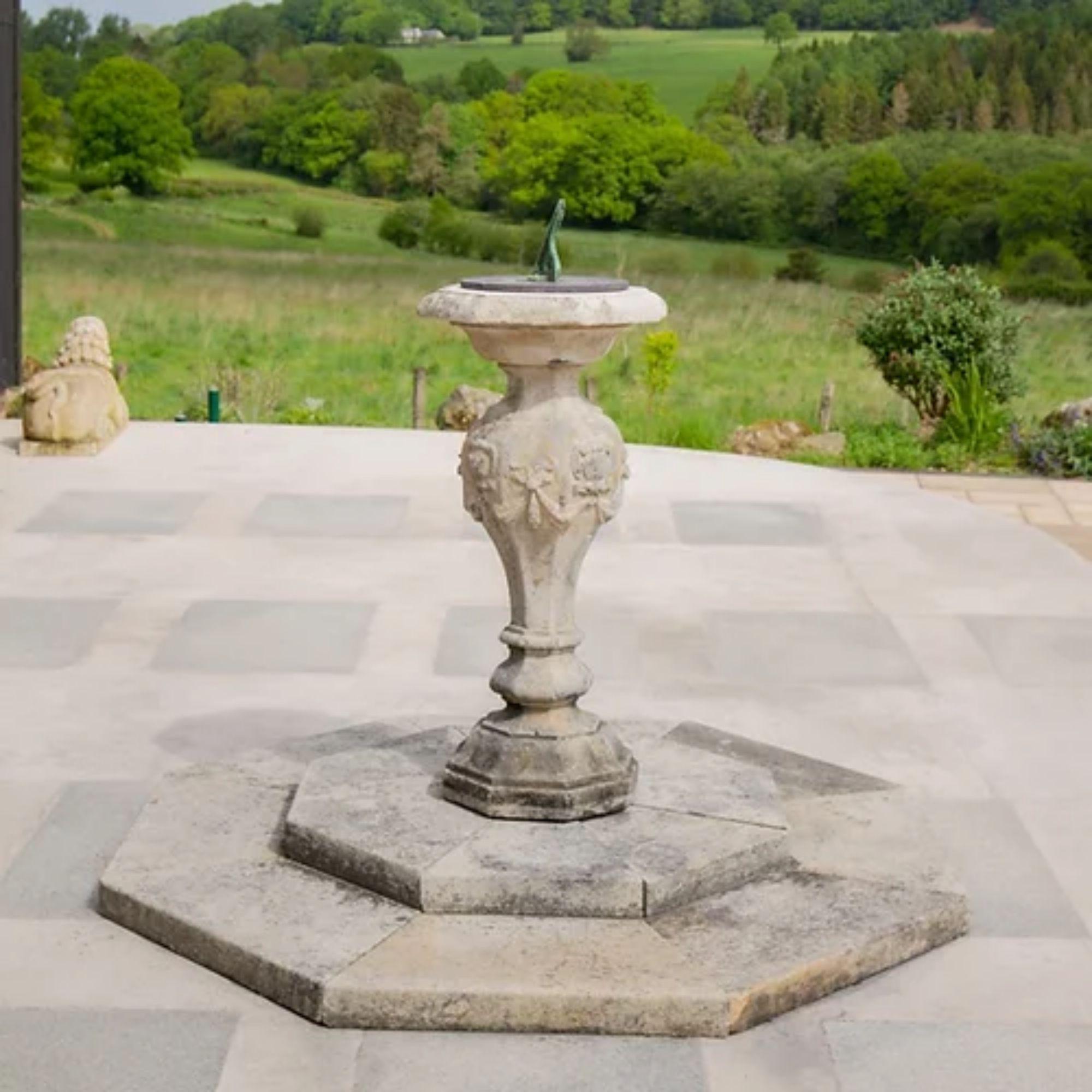 A rare 18th century stone sundial of large proprtions decorated with cartouche and swag ribbon detail, standing on a substantial stepped octagonal base. The pedestal retains the original slate plate complete with large bronze gnomen, circa