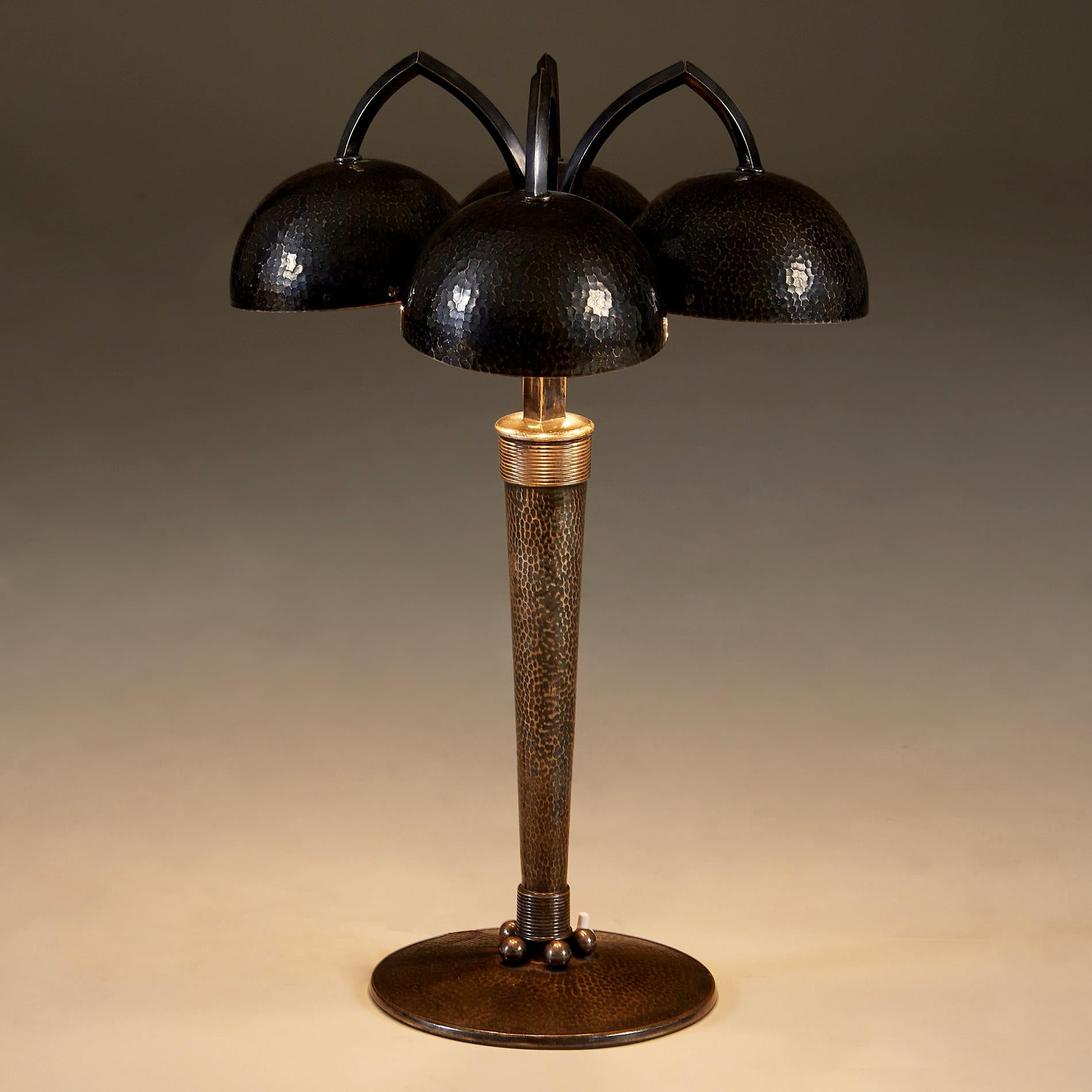 An extremely rare table lamp by two French design masters. This perfectly proportioned hammered metal table light is wonderfully refined in detail and finish. Four hammered metal shades hang from arched metal arms. These are supported by a tapered
