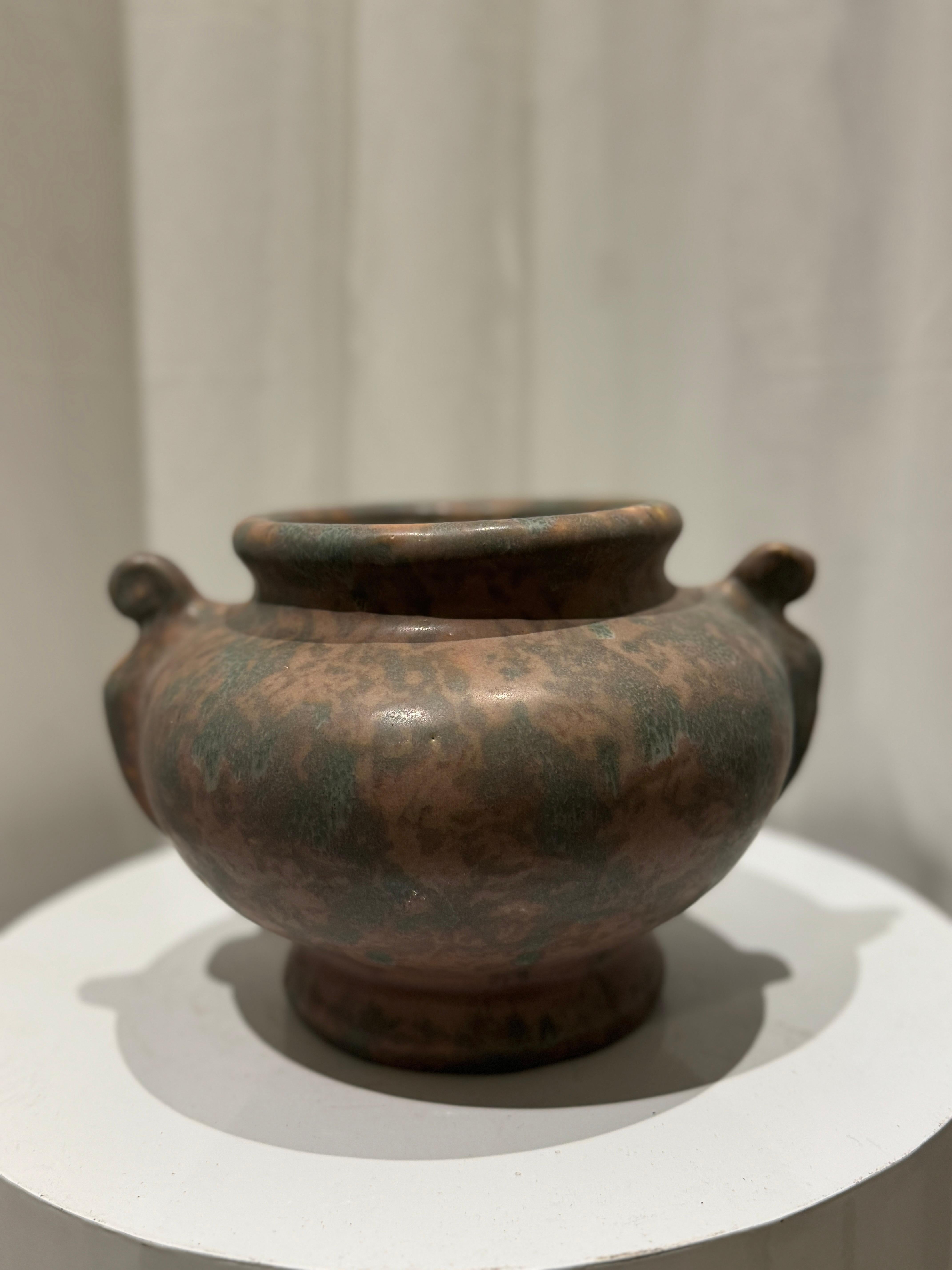 Questo squisito vaso con manico di Weller Pottery Art Vellum del 1930 rappresenta il meglio della ceramica americana dei primi del Novecento. Caratterizzato da una smaltatura morbidamente screziata di verdi e marroni, questo pezzo artigianale