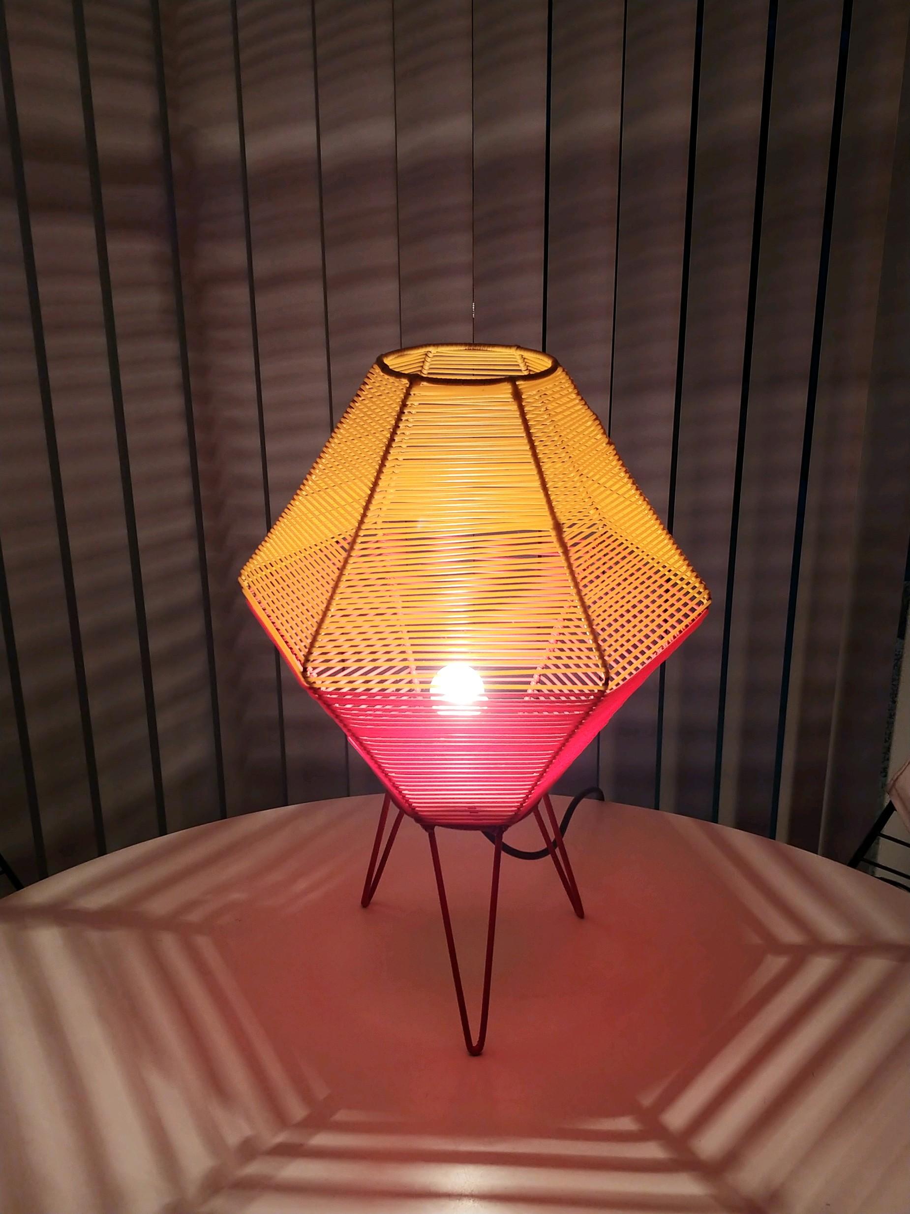 This wire frame lamp with hairpin legs is wound with red and yellow nylon cord. When used with a clear bulb the light creates patterns on the table and on the walls. Nylon cord is 100% with no losses or damage. This lamp was found in Germany and is