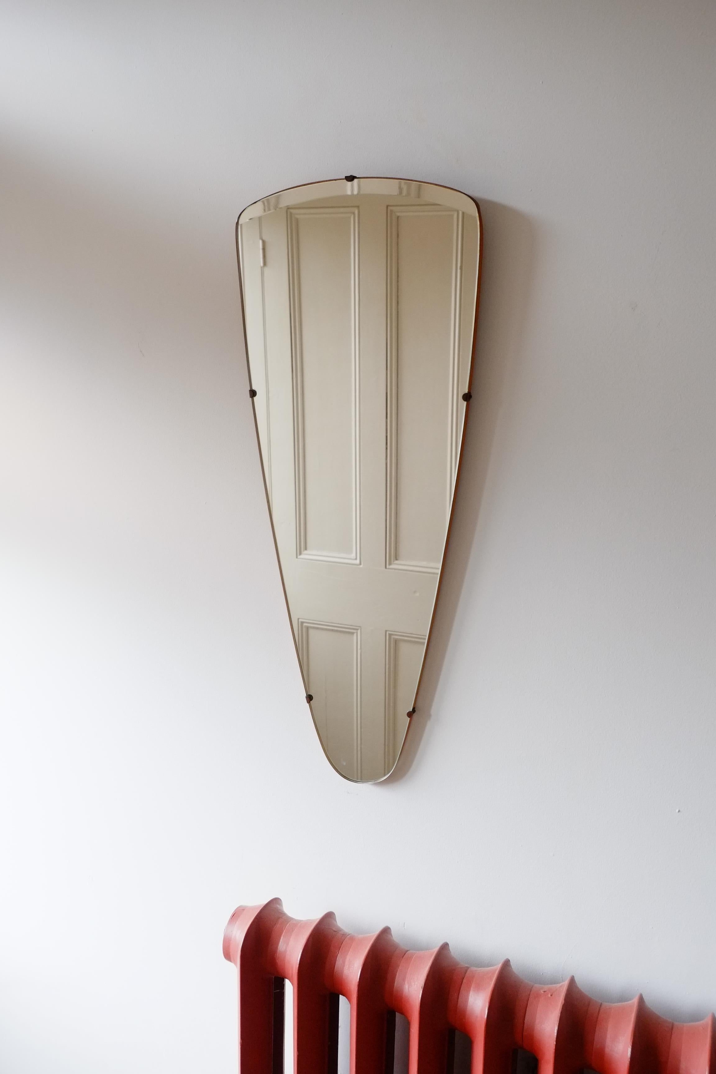 A rare midcentury triangular mirror. The mirror has a gorgeous minimal style, with a frameless glass, wooden back and metal clasps at the edges. I haven't seen this wedge shaped triangle shape often and this one is particularly nice as it has a