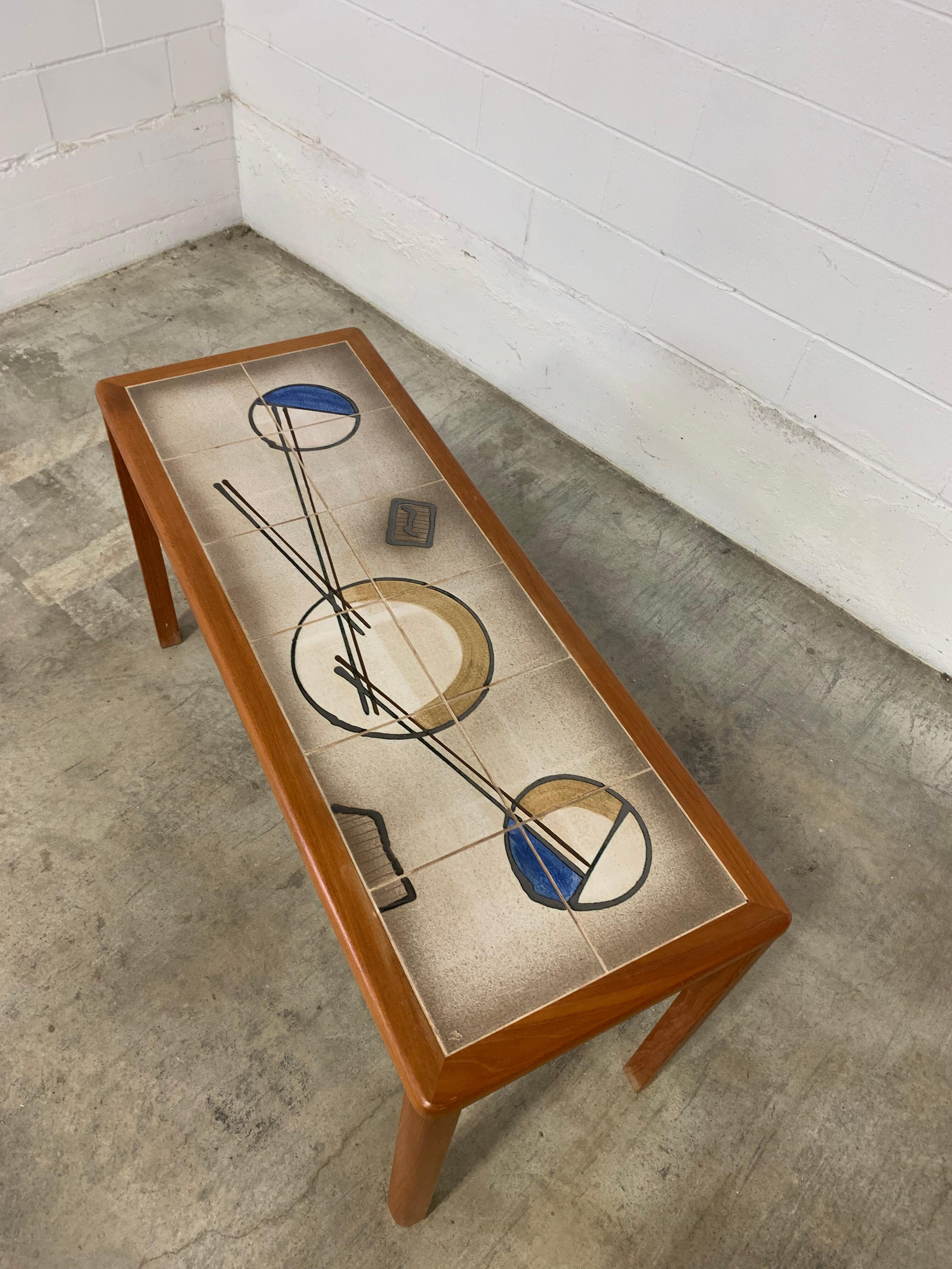 A rare 1970s Danish teak and tile console table with bold, modernist flair. The inset ceramic tiles feature a one-of-a-kind abstract motif in earthy neutrals, ochre, and cobalt—no other like it exists. Measuring 52” wide, 20” deep, and 28” high, it