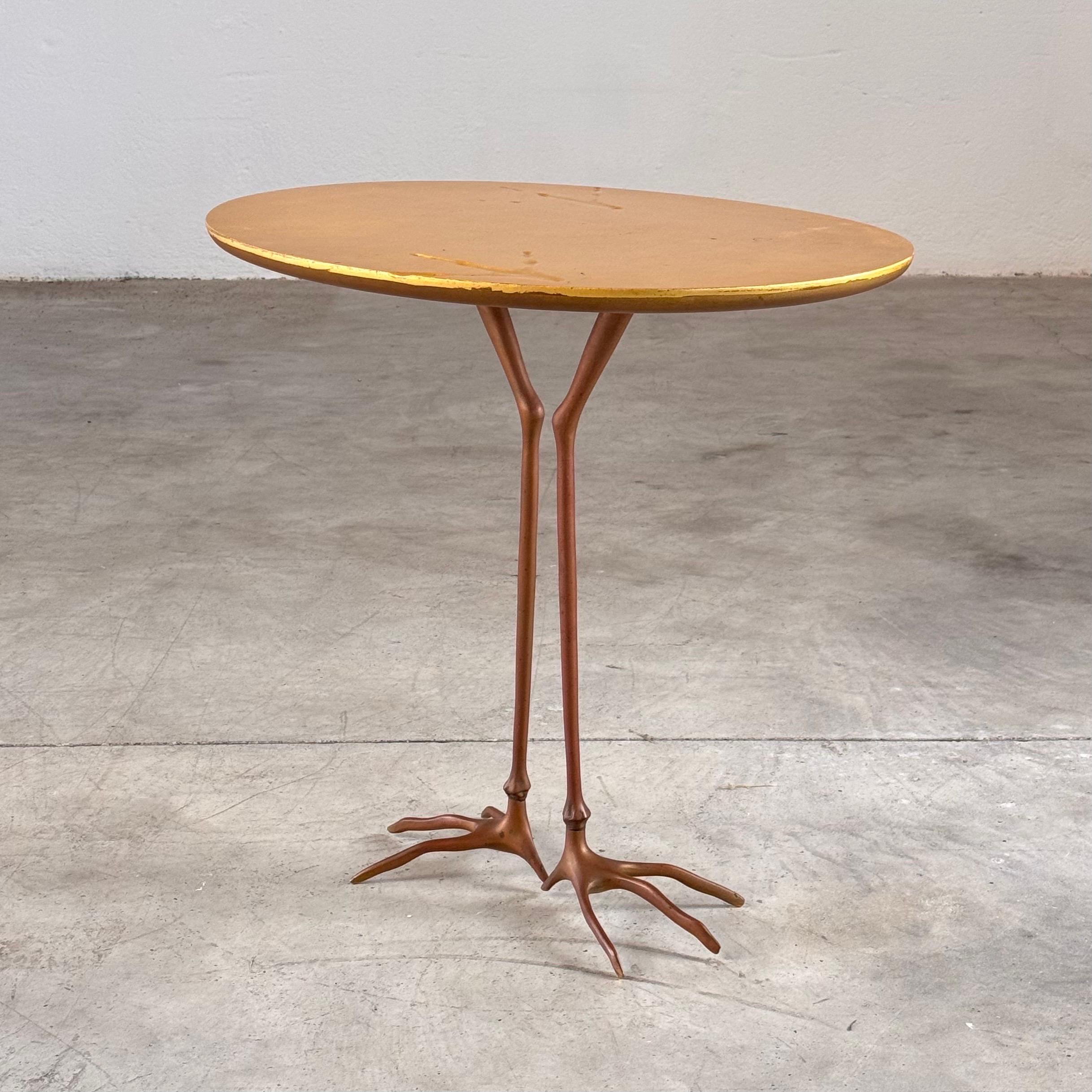 Cette table rare et emblématique présente un plateau en bois recouvert de feuilles d'or avec des traces d'oiseaux en relief sur toute la surface. Il repose sur deux pieds sculpturaux en laiton massif, en forme de pattes d'oiseau.

Le design a été