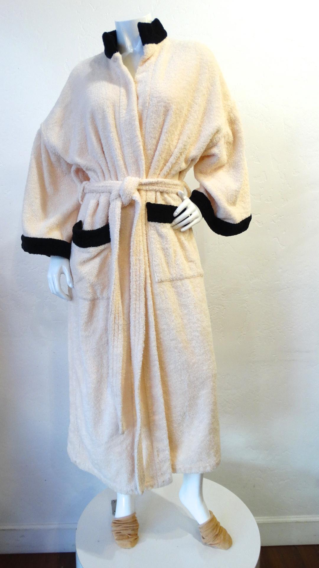 Relax In Style With This Chanel Bath Robe! Circa 1990s, this adorable soft pink terrycloth robe features black trim around the collar, billowy sleeves and on the two front square pockets. The iconic Chanel CC is included on the back. The perfect