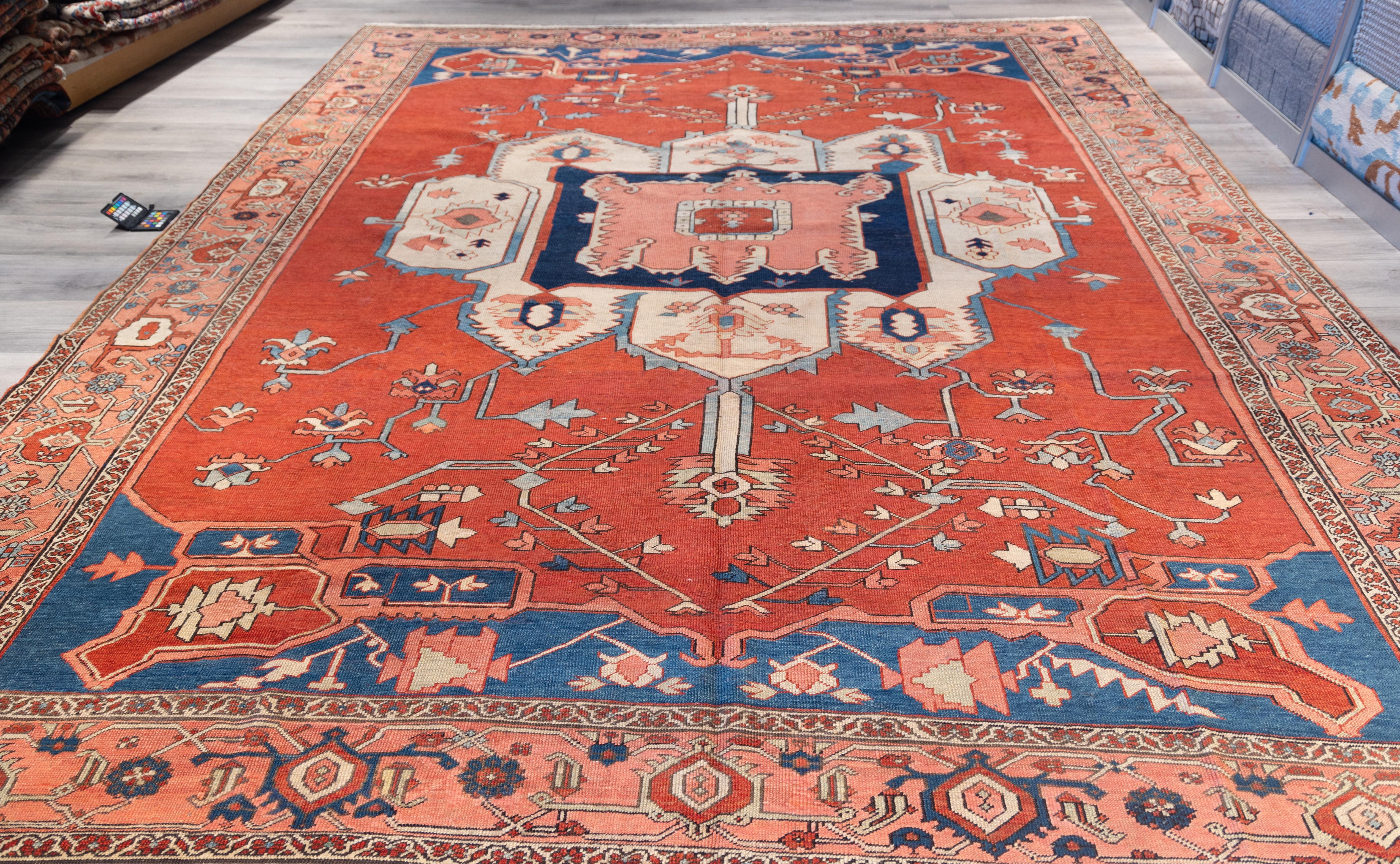 A striking Serapi ,  featuring a bold geometric medallion set against a rich brick-red field. The central medallion, rendered in soft ivory, deep navy, and pale blue, is flanked by stylized corner spandrels that echo the medallion’s angular motifs,