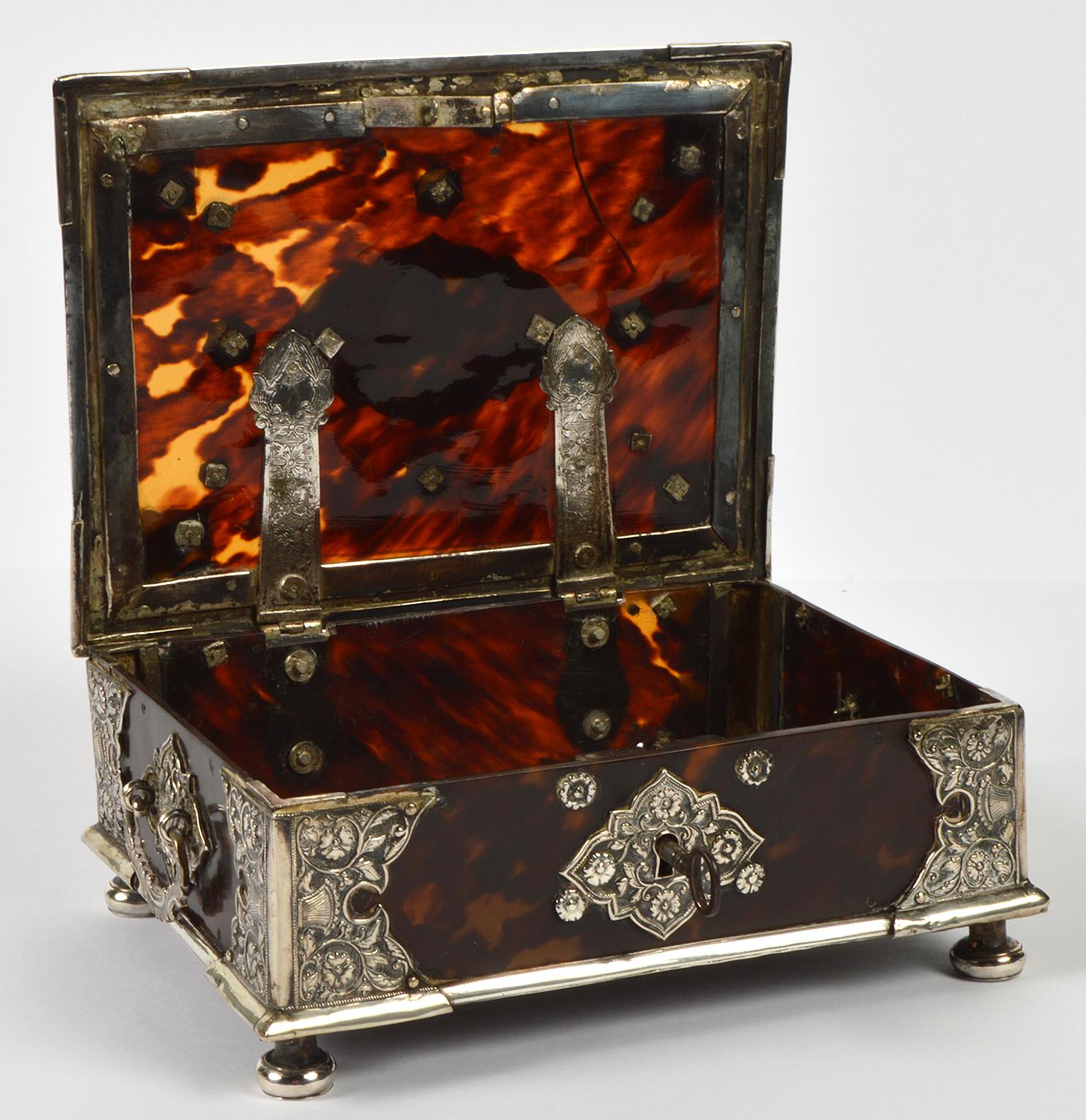 Standing on prolonged silver bun feet this magnificent box features a body of tortoiseshell, engraved hinges, handles and repousse silver mounts and plaques combined with straight silver bands. The decorative patterns depict flowers, leafwork and
