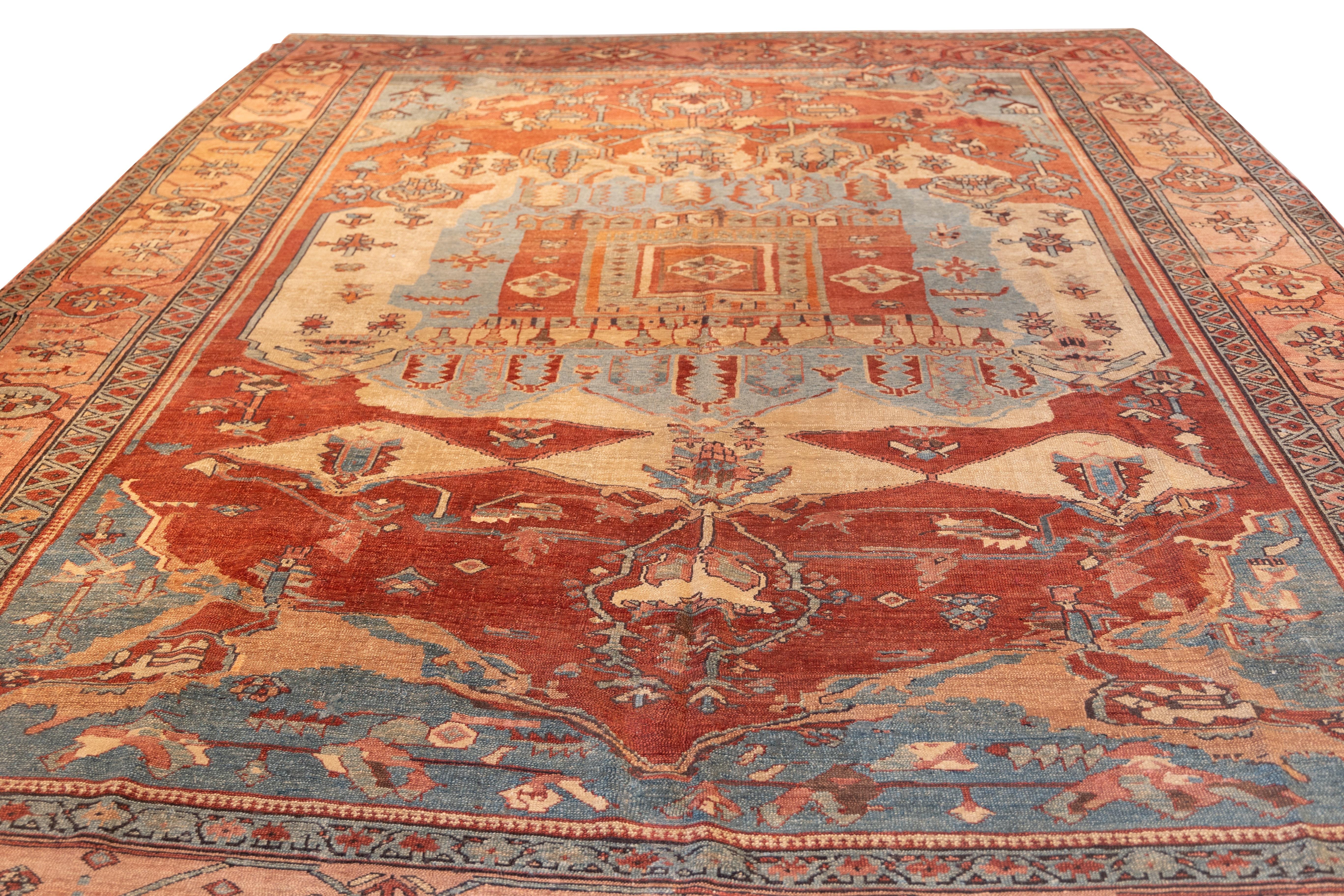 The design centers on a grand stepped medallion with a palmette and cruciform motif, framed by a balanced array of angular vines and stylized floral elements. The surrounding field, rendered in a harmonious blend of rust, pale blue, and soft ivory,