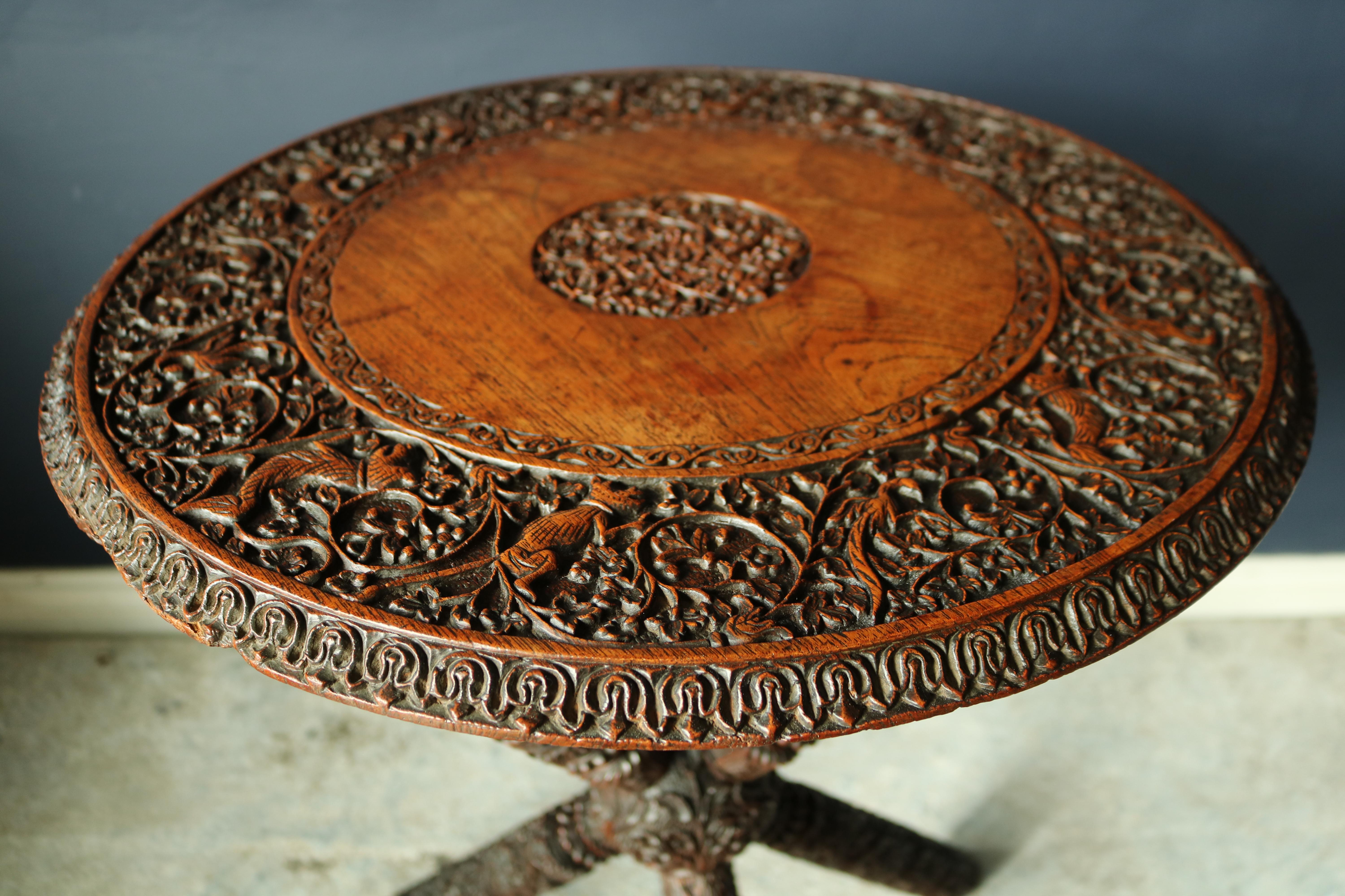 A rare 19th century Burmese carved tripod table, with profusely carved decoration of foliage and jungle animals in the traditional fashion carved from very high quality Burmese teak standing on a very unusual tripod base.
             