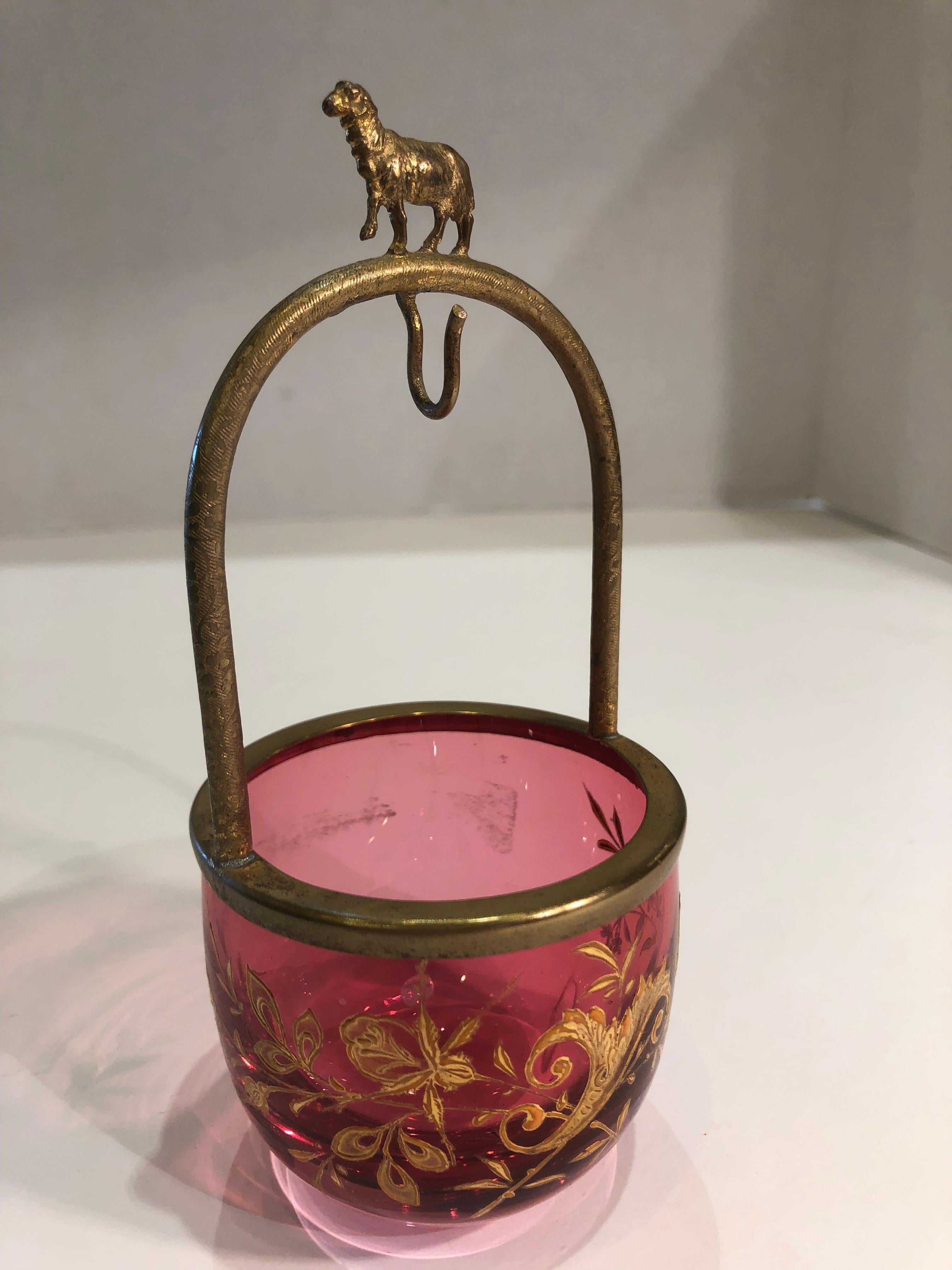 Beautifully handcrafted, arched display stand from which to hang a pocket watch features a gold metal frame and hook with an arch decorated with a whimsical sheep.  This frame is attached to a light cranberry colored glass multipurpose trinket dish,