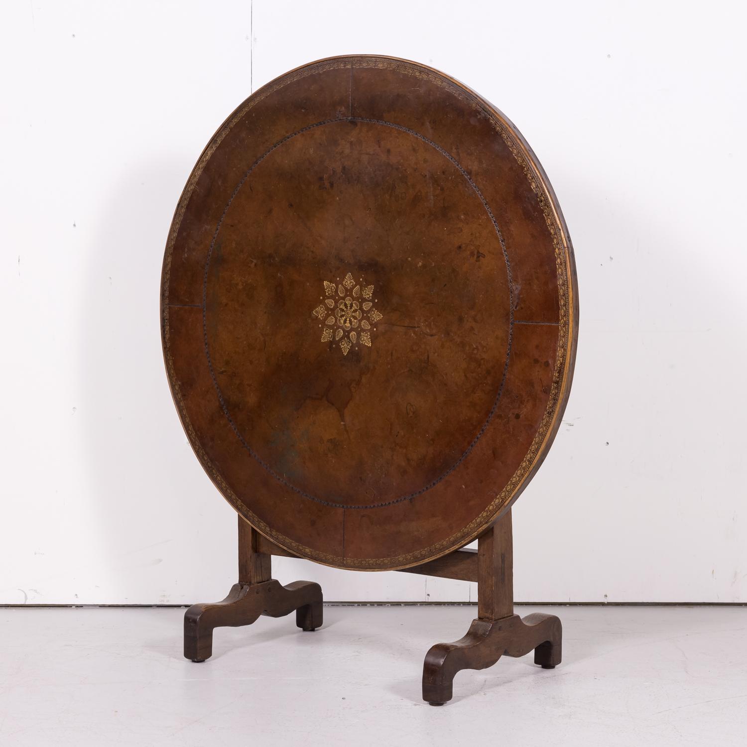Rare 19th century French Charles X period tilt-top vendange or wine tasting table handcrafted of old growth oak near Beaujolais, having the original circular brown and gilded tooled leather top with richly patinated oak border, circa 1820s. Raised