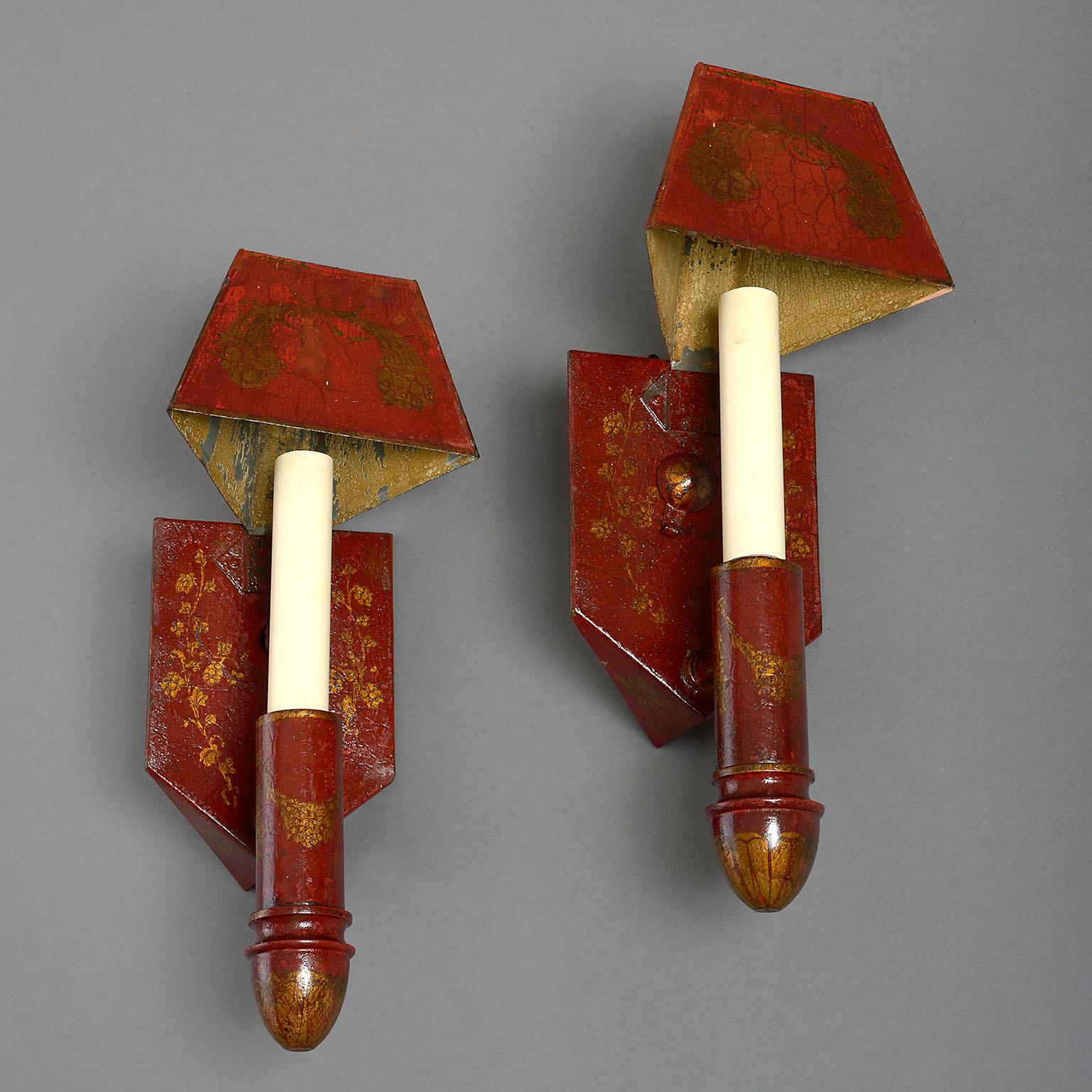A rare pair of early 19th century red tole corner wall lights. The shield-shaped reservoirs with projecting arms fitted for electricity and supporting tapering triangular shades, all painted with cornucopia and trailing vines on a sealing-wax red