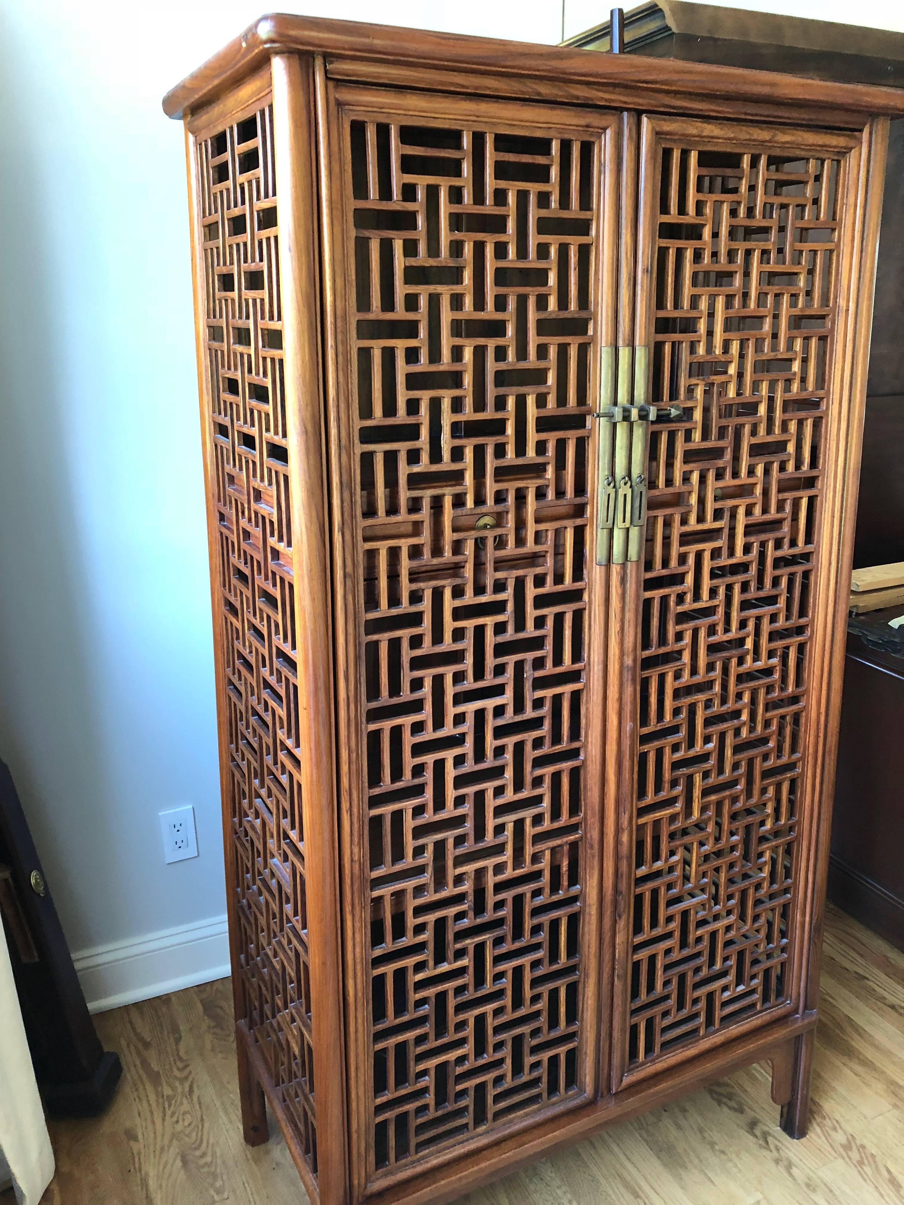 A beautiful and versatile open lattice cabinet in gorgeous Huanghuali hardwood, having Asian style hardware with two doors that open to shelves and two drawers inside.
Purchased in Singapore about 25 years ago from Tomlinson Antique House.