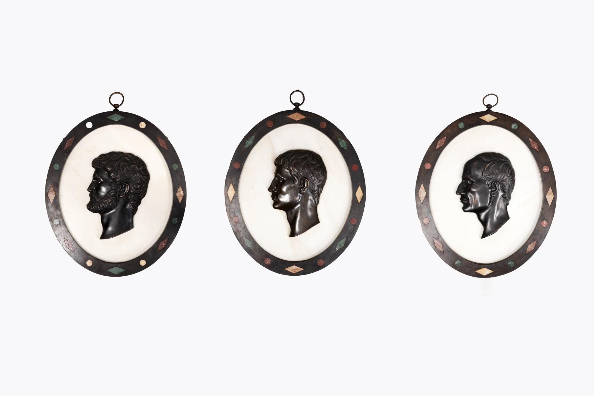 Rare 19th Century set of three unusually large Grand Tour oval Carrara marble plaques featuring relief profiles in bronze of Julius Caesar, Caesar Augustus and Hadrian. All three are enclosed by specimen samples of precious stone inset in black