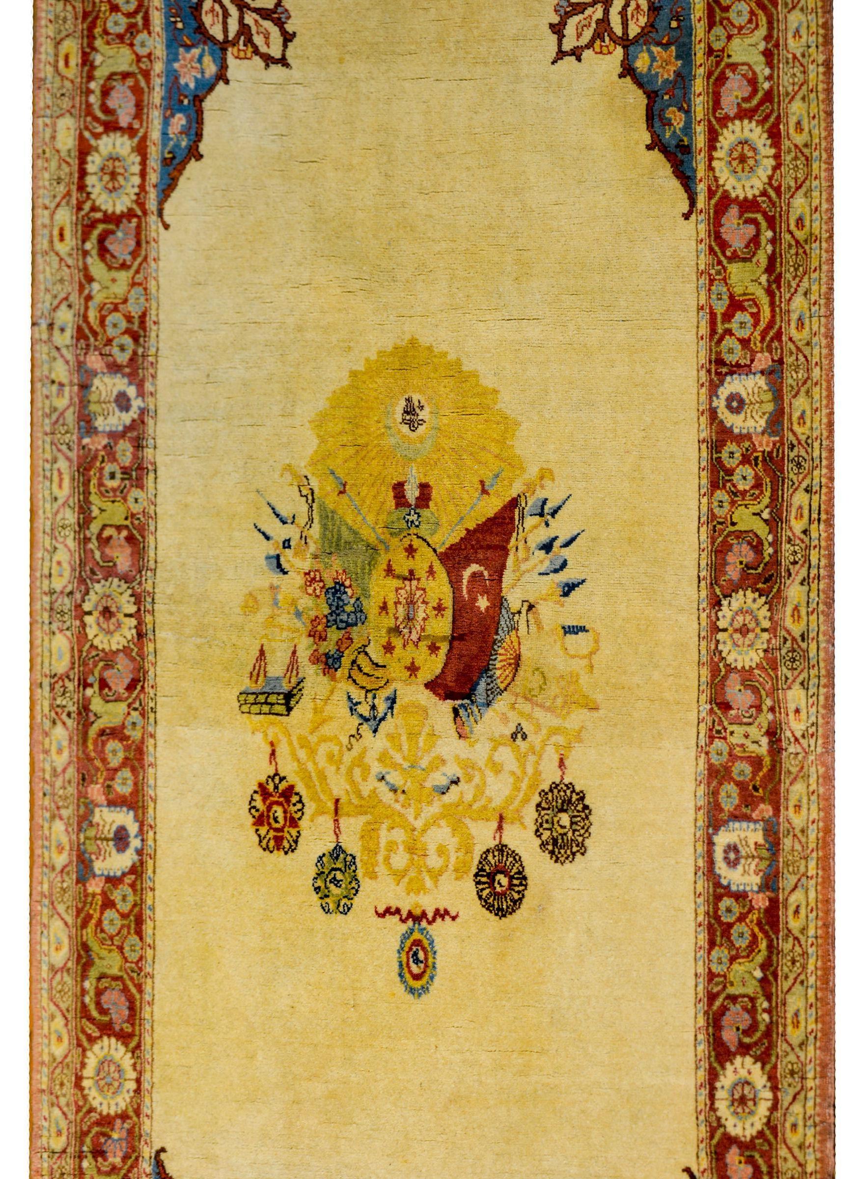 A rare 20th century Turkish Hereke rug with a gorgeous pale yellow field with a large central coat of arms of the Ottoman Empire. The emblem features an ornate cartouche surrounded by various elements of the state including two flags. The red flag