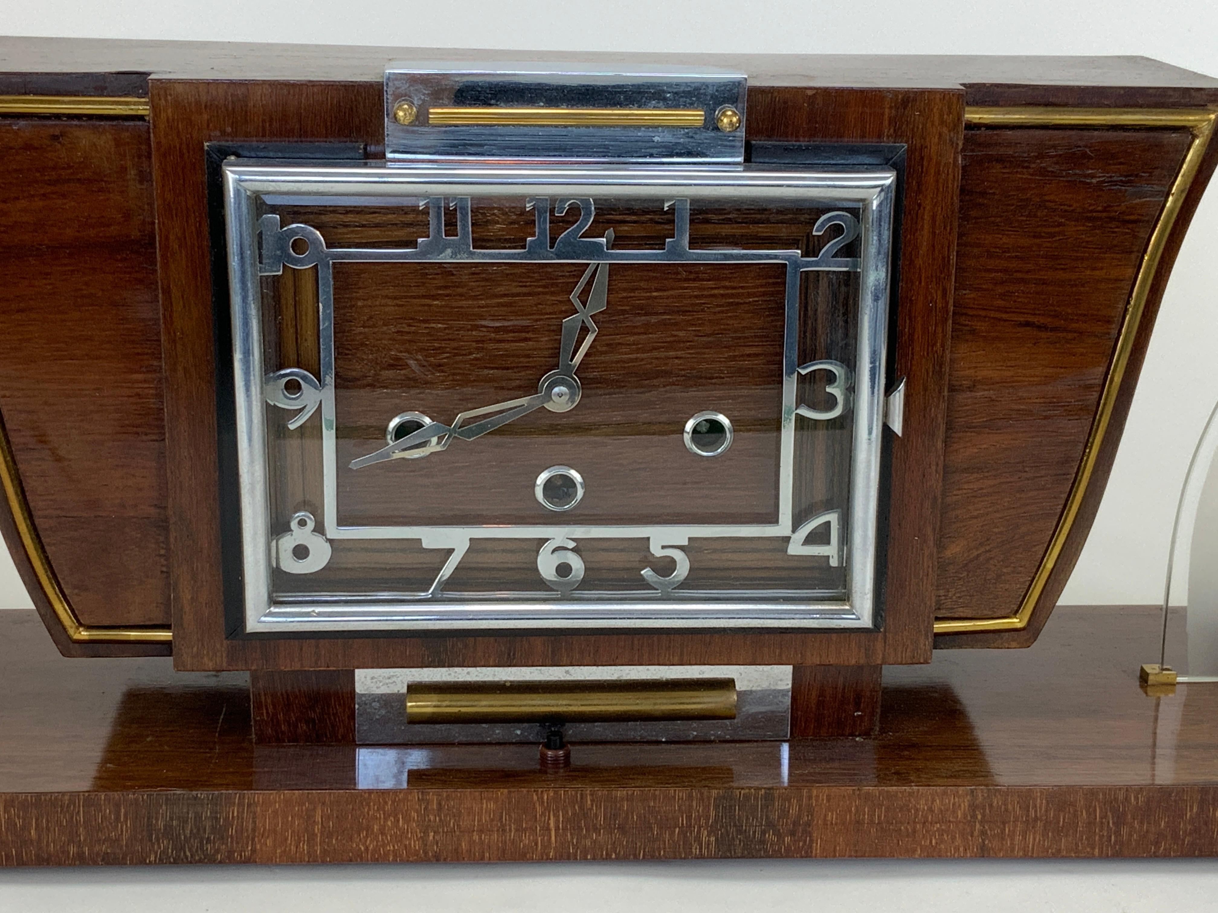 Une rare et magnifique pendule de cheminée Art Déco avec des lumières côte à côte.  Le boîtier et la base sont recouverts d'un placage de bois exotique typique des designers et fabricants français de l'Art déco. Il est rehaussé d'une garniture en