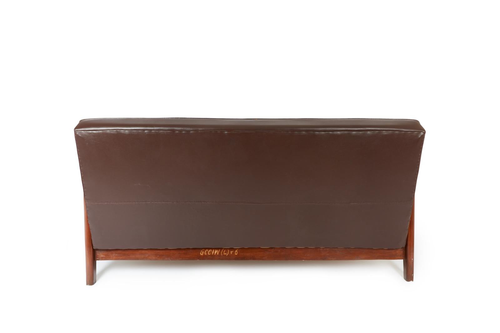 Rare sofa in teak and faux dark brown leather from the High Court of Chandigarh (Sector 1, Capitol Complex) designed by Pierre Jeanneret and Le Corbusier. 
This model has a slightly sloping backrest and a solid bridge structure. 
According to expert
