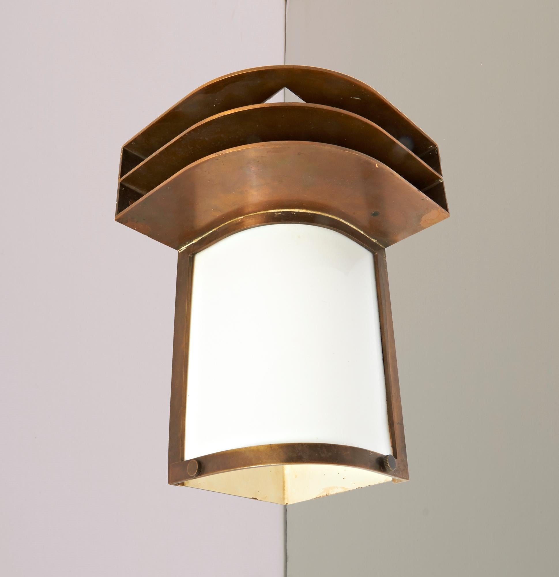 This spectacular American Art Deco/Machine Age is a real statement piece. It is a solid bronze wall sconce designed to be mounted in a corner with the light emanating from a curved milk glass panel inset at the front and additional light shining