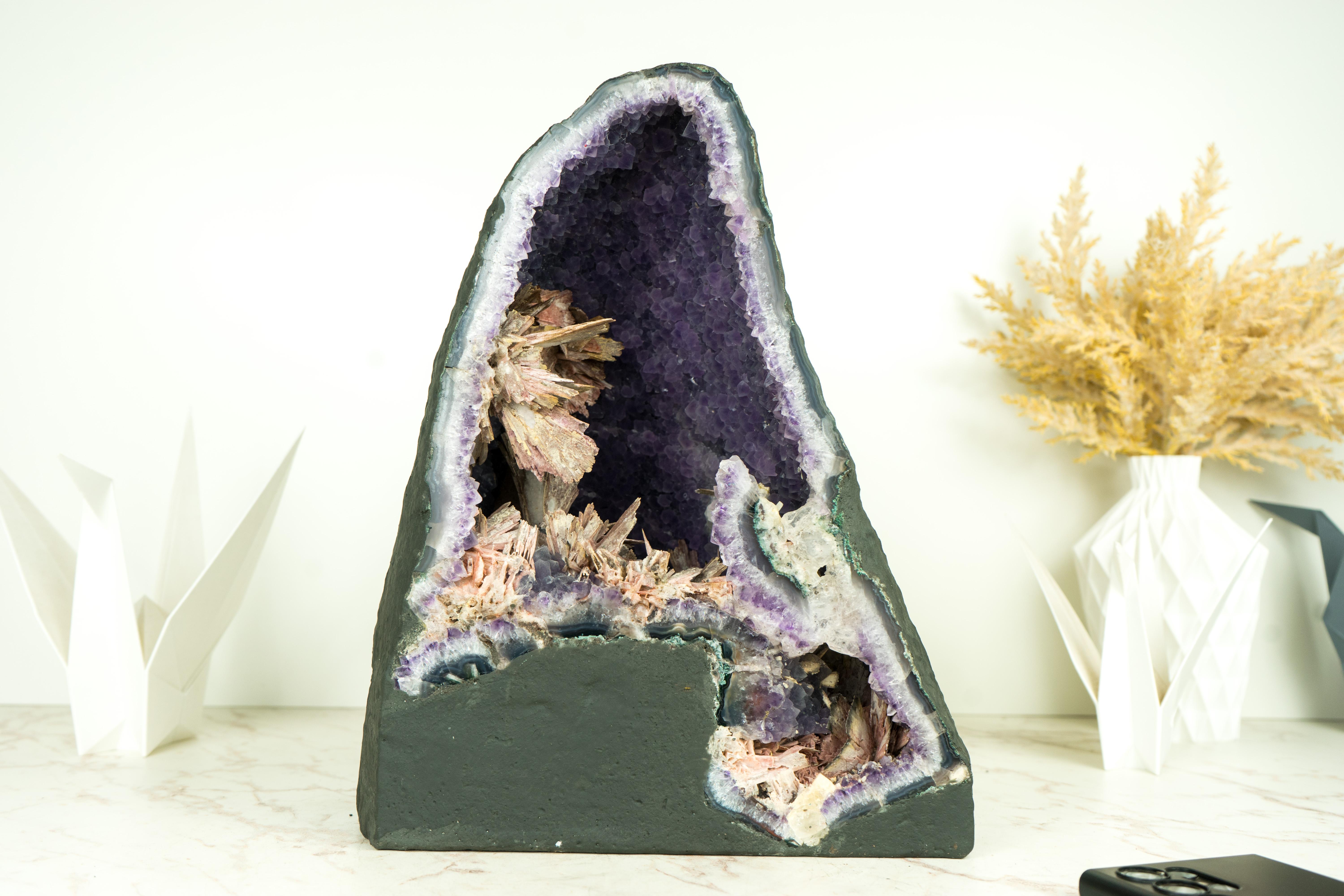 Elegant and sculptural, this geode showcases some of the rarest elements found in any Amethyst. It features world-class Pink Pseudomorph flowers growing atop a beautiful, high-grade, second-generational Amethyst druzy. This specimen is a superb