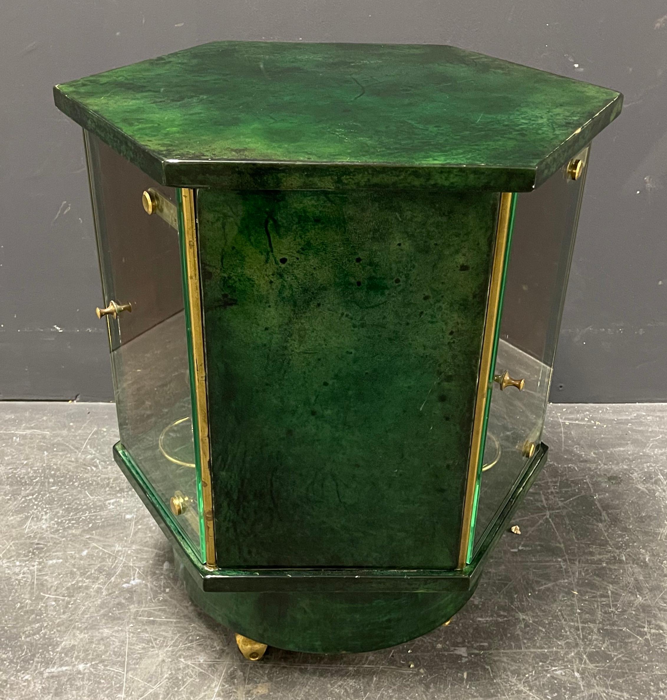 Elegant Aldo Tura bar cart on brass wheels in hexagonal shape with three glass doors and a rotating bottle holder inside.