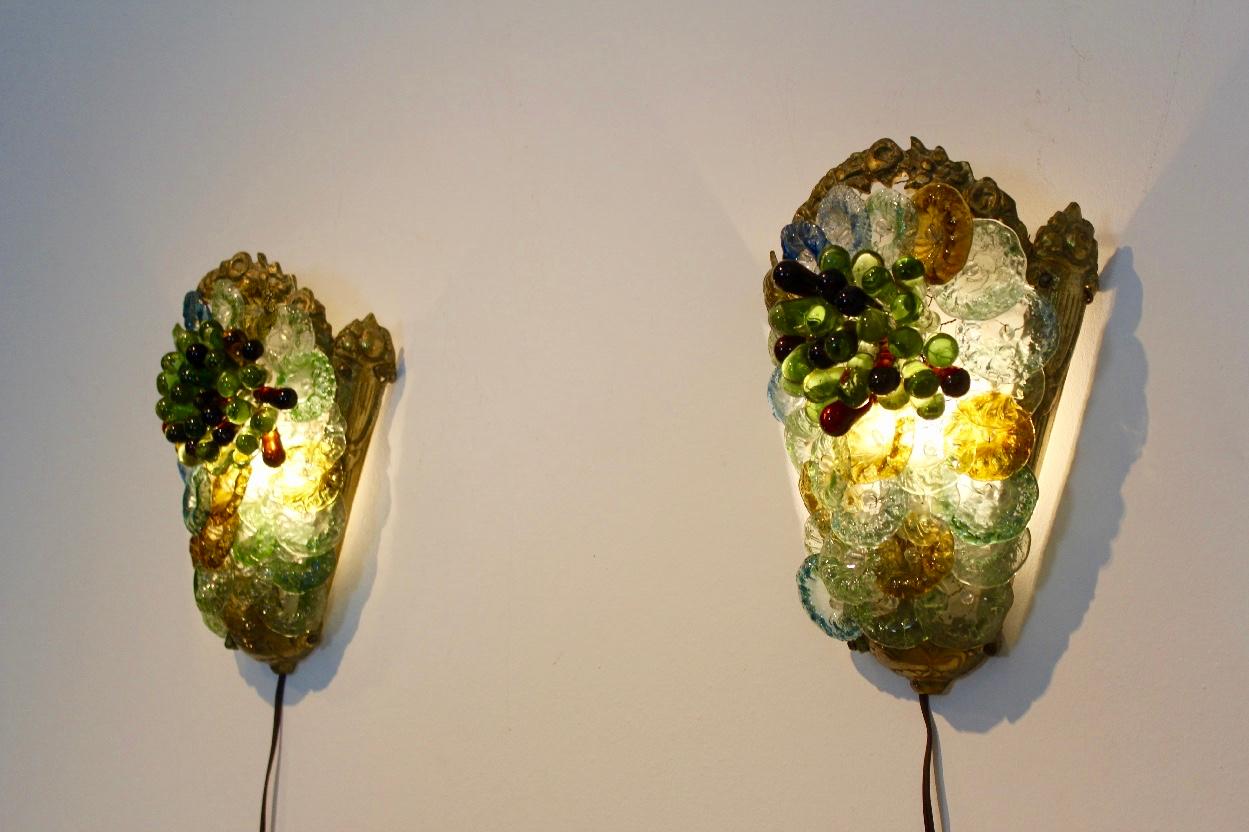Highly sophisticated and rare pair of brass and Murano glass sconces produced in Italy in the 1950s. Each lamp has a handsome Brass frame with colorful Murano Glass in the shape of beautiful Flowers and Grapes. Consisting of many transparent, green,