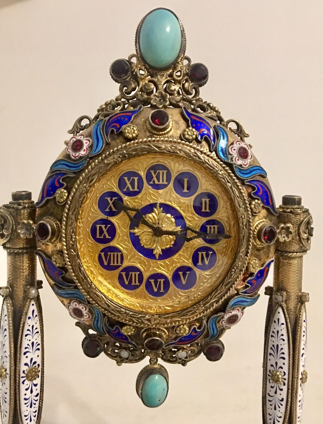 A rare and fine Viennese silver gilt, enamel, pearl and semi precious stone mounted musical table clock of portico form, the circular case surmounted by an oval cabochon of turquoise stone, raised on a pair of columns terminating in pierced bases