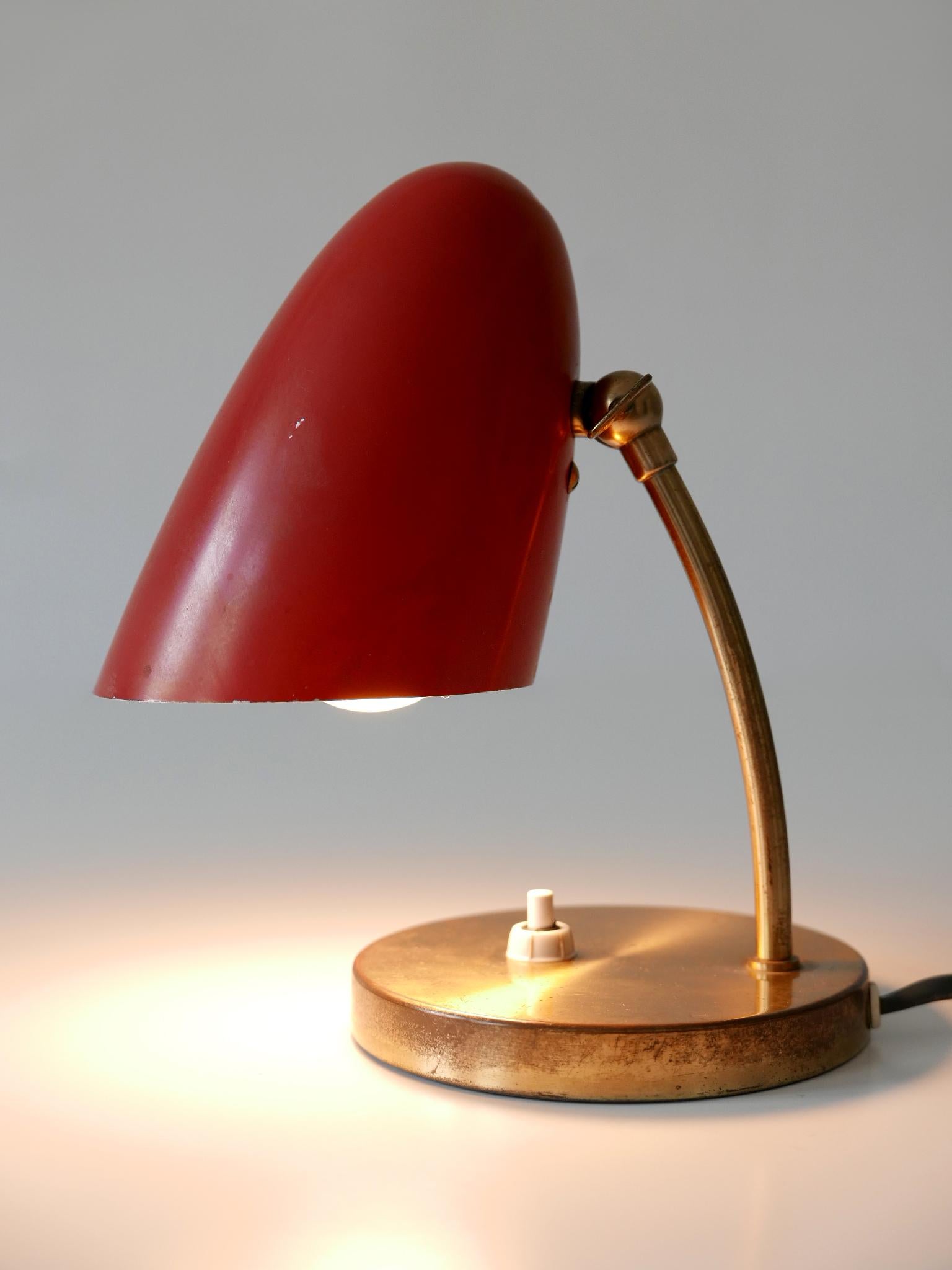 Elegante et très décorative lampe de table Modern-Decor avec abat-jour ajustable. Conçue et fabriquée en Allemagne, dans les années 1950.

Réalisée en aluminium émaillé rouge, en laiton et en métal, la lampe est livrée avec une douille à vis