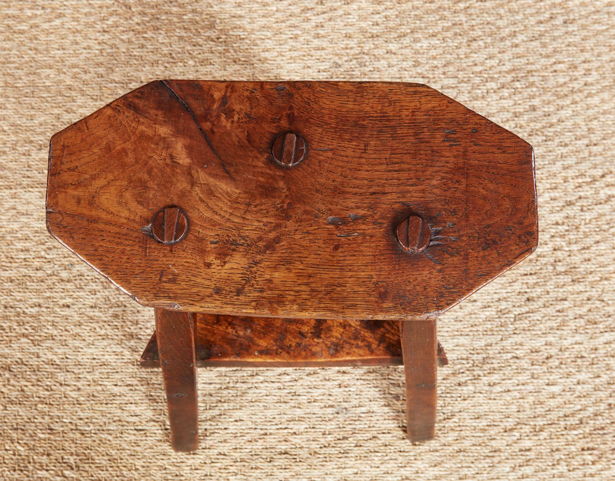 Un grazioso e raro tavolino da charme in olmo lucido, con un piano ottagonale oblungo e spesso con un sottopiano triangolare, sostenuto da tre gambe sbozzate. Grazie alle sue dimensioni ridotte, è adatto come tavolino per bevande facilmente
