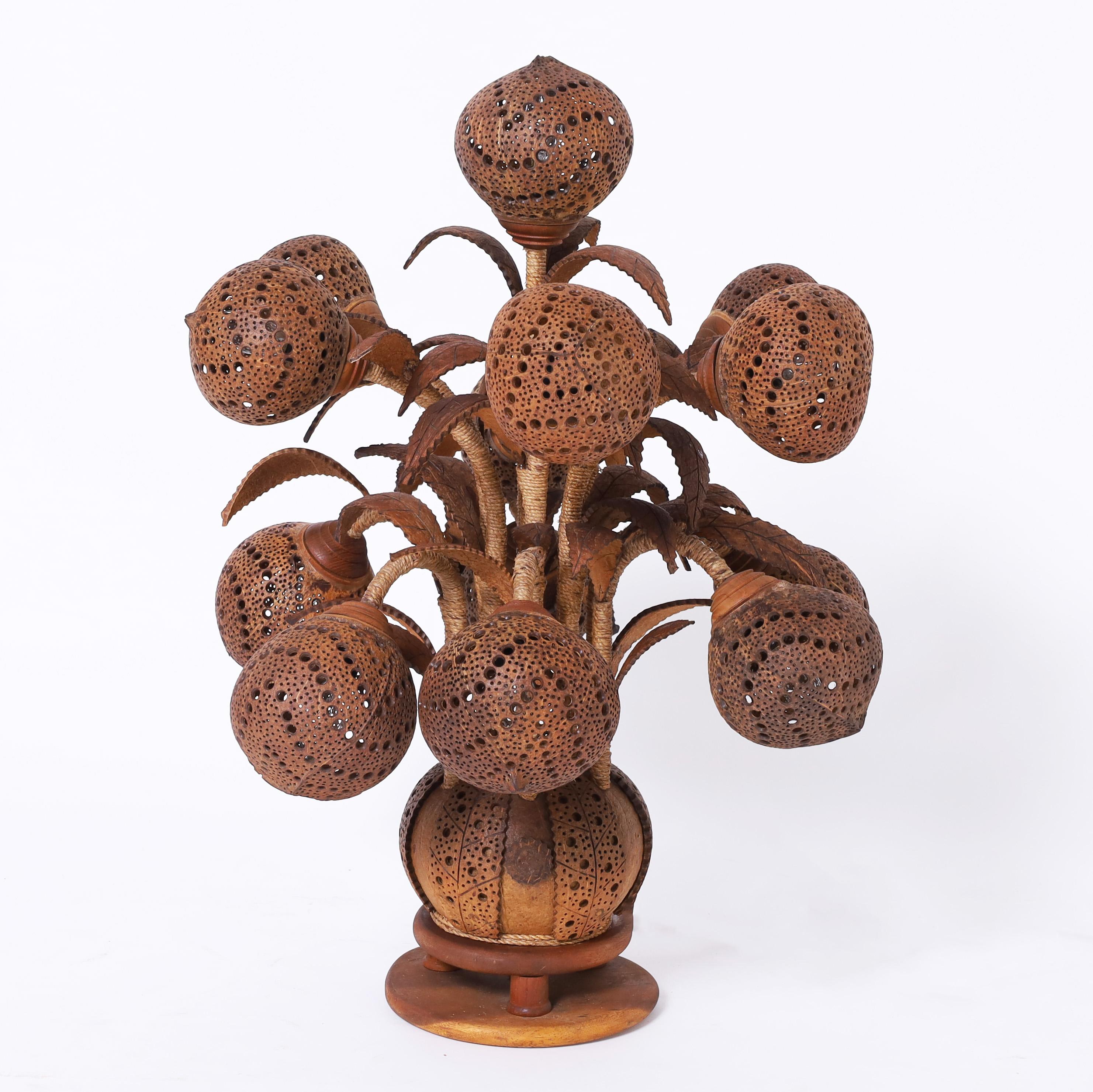 Rare and unusual handmade table lamp featuring thirteen carved and perforated coconut shells as shades, carved coconut leaves, hand wrapped string stems and a coconut base on a mahogany platform. 