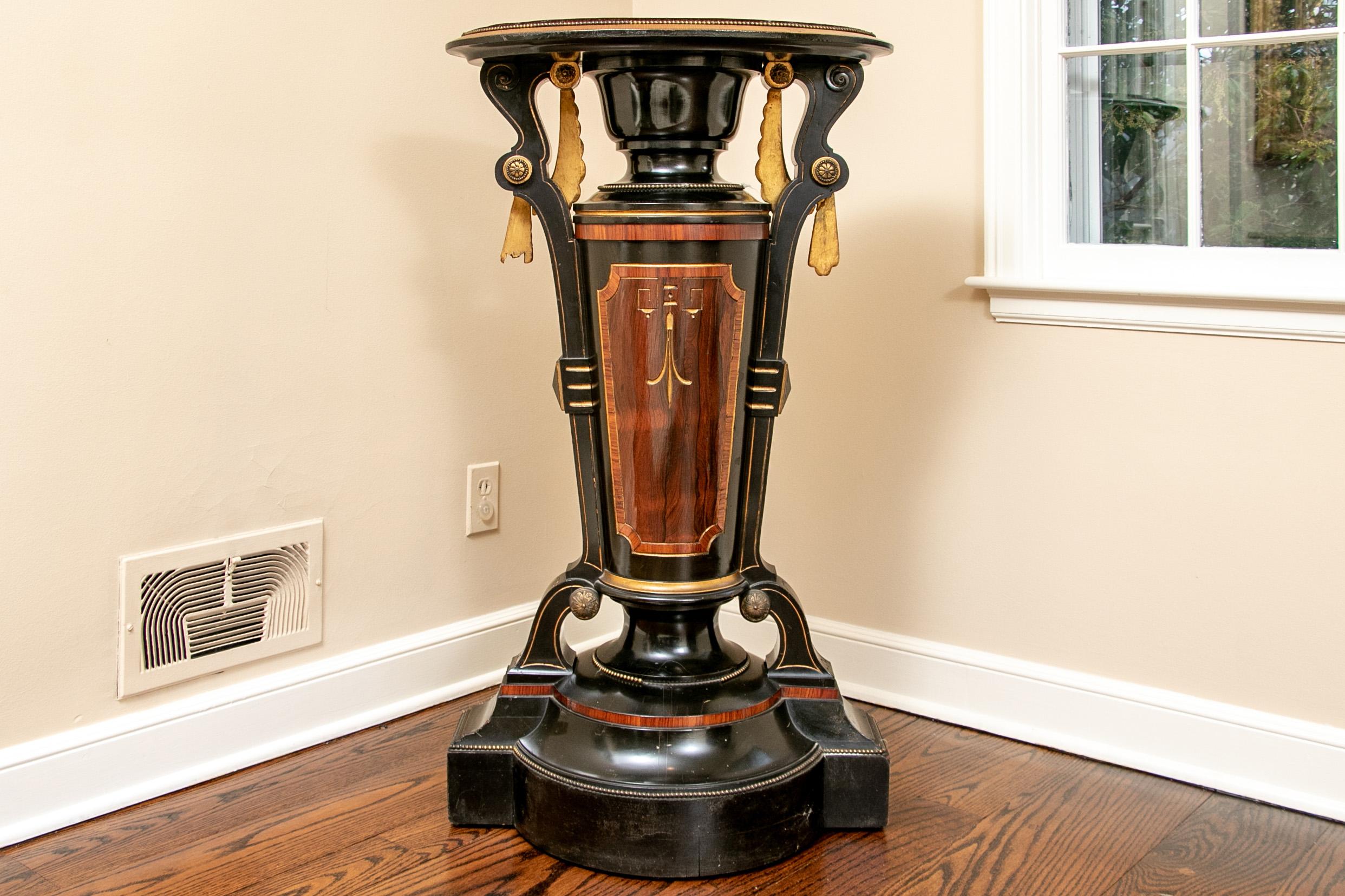 A very decorative and elaborate display pedestal that’s rare and very desirable. An antique oval velvet covered top sits astride an elongated hourglass form base that is ebonized and further decorated with gilt swags, rare wood accents, beading and