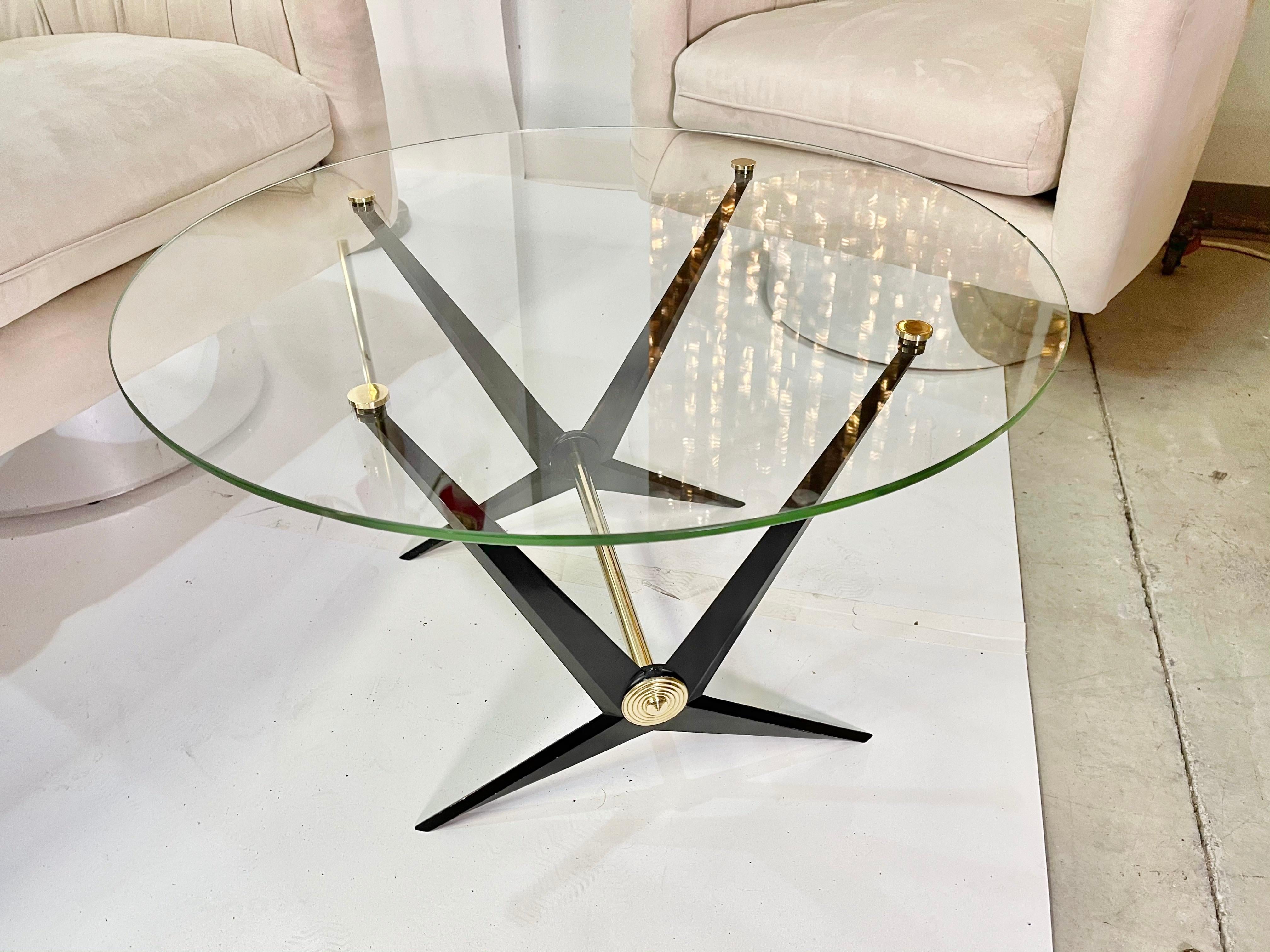 Chic round coffee table by Angelo Ostuni. Angular black enameled aluminum frame with brass embellishments. Attached round glass top is pierced and capped with four round brass caps.