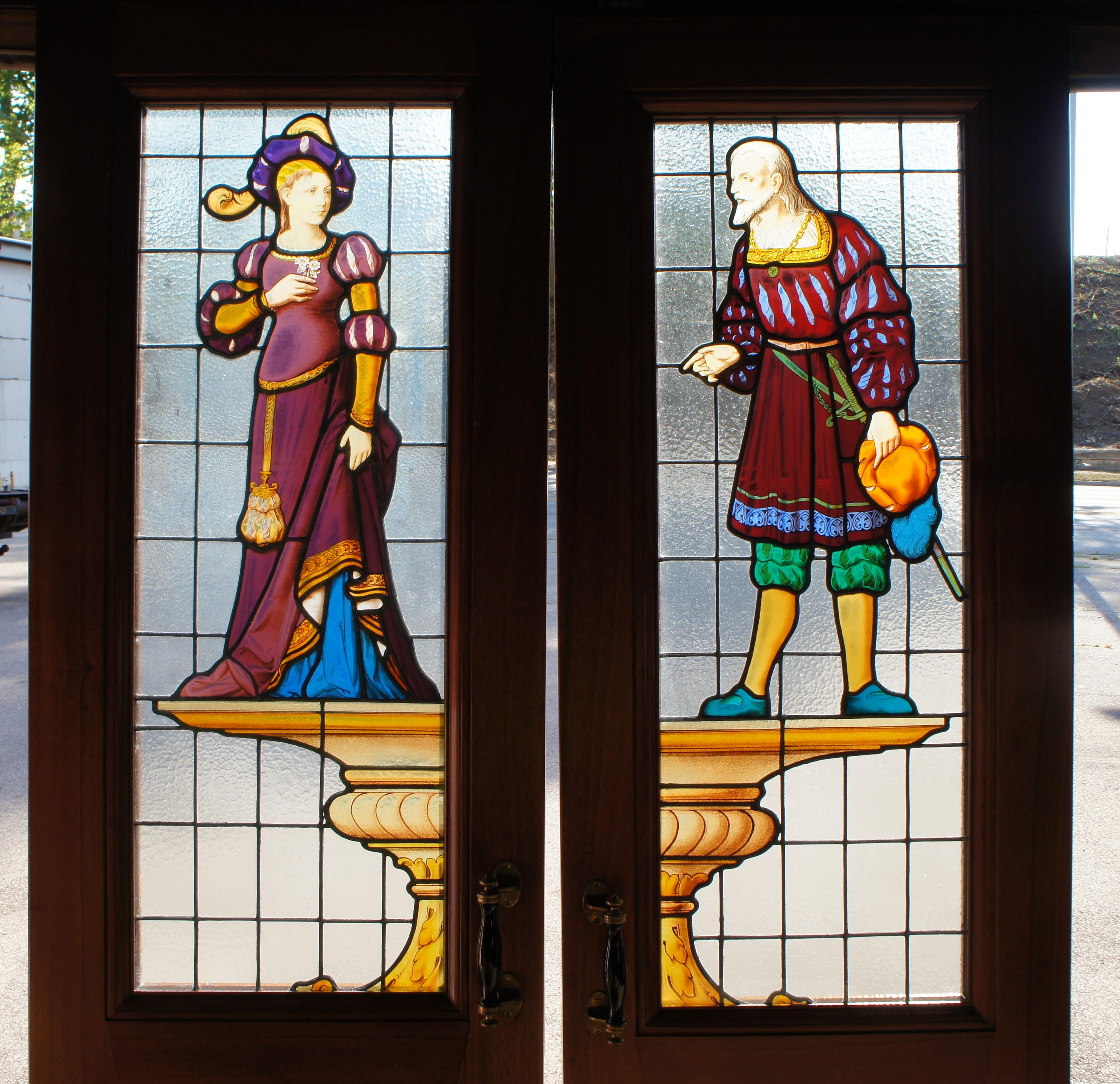 A monumental set of Renaissance Revival figural leaded stained glass French / double doors of the highest quality. Features a nobleman courting a lady. Both are poised on top of a Doric or Roman capital in traditional attire facing each other. The