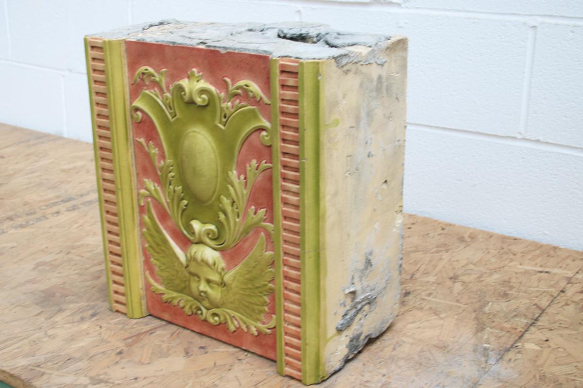 Rare Burmantofts architectural tile block. The central tile panel is in high relief showing a cherubs head and wings below a large unadorned cartouche. This panel is flanked by two laddered edge tiles. 

Overall 39 cm wide x 42 cm high x 23 cm