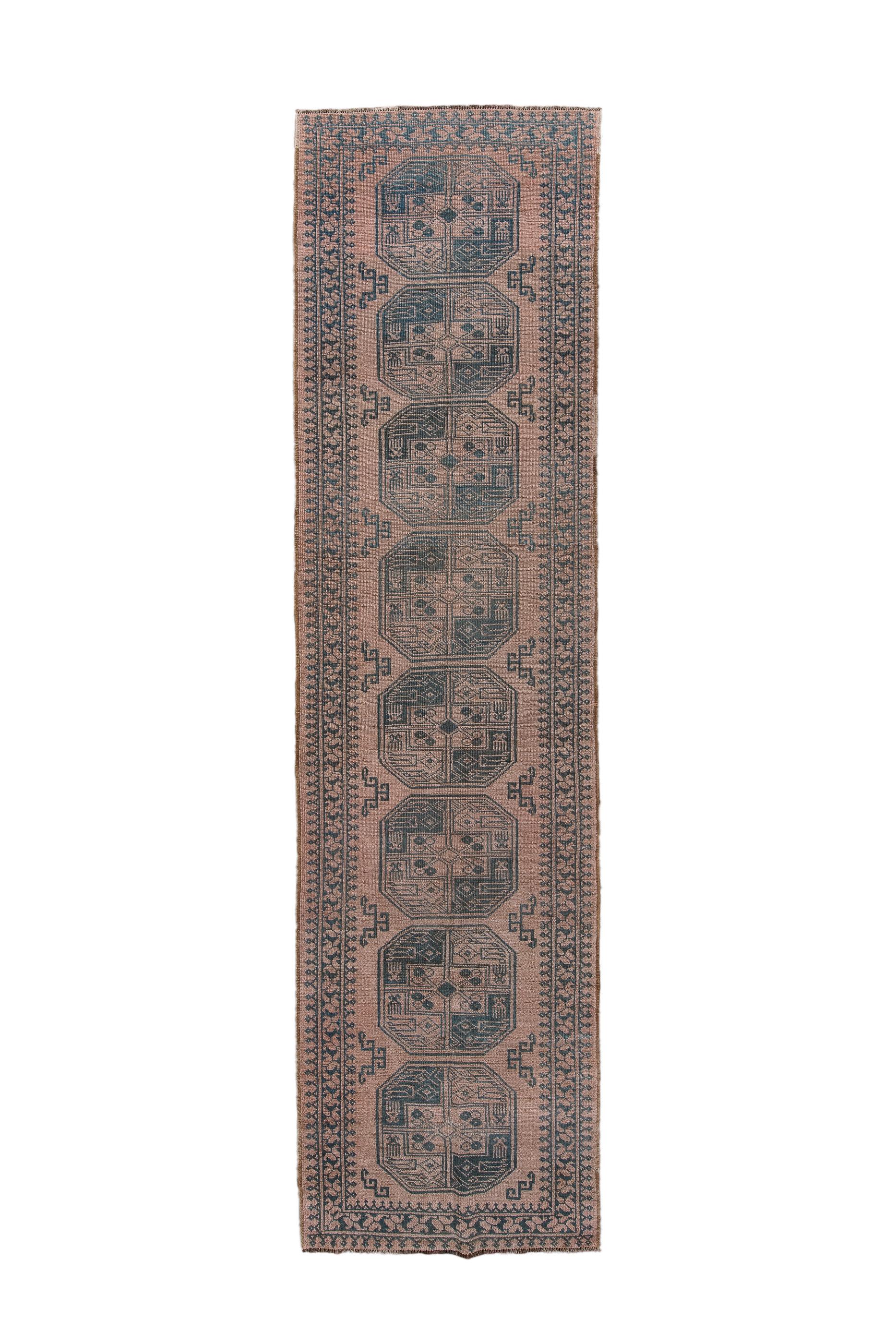 This is a relatively unusual Afghan format – a runner – with a light brown field supporting eight large, octagonal  emblematic tribal guls, with discrete fractional minor guls at the sides. Field edged with triangular turrets and a main skinny