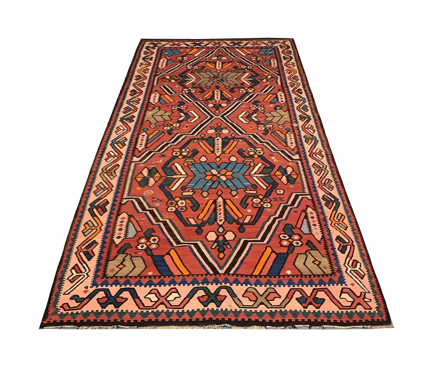 This handwoven antique Kilim was constructed in 1920 with fine hand-spun wool. The design features a double medallion in the centre and a detailed surround with smaller motifs and a repeat pattern border. The pattern is woven on a rust-red
