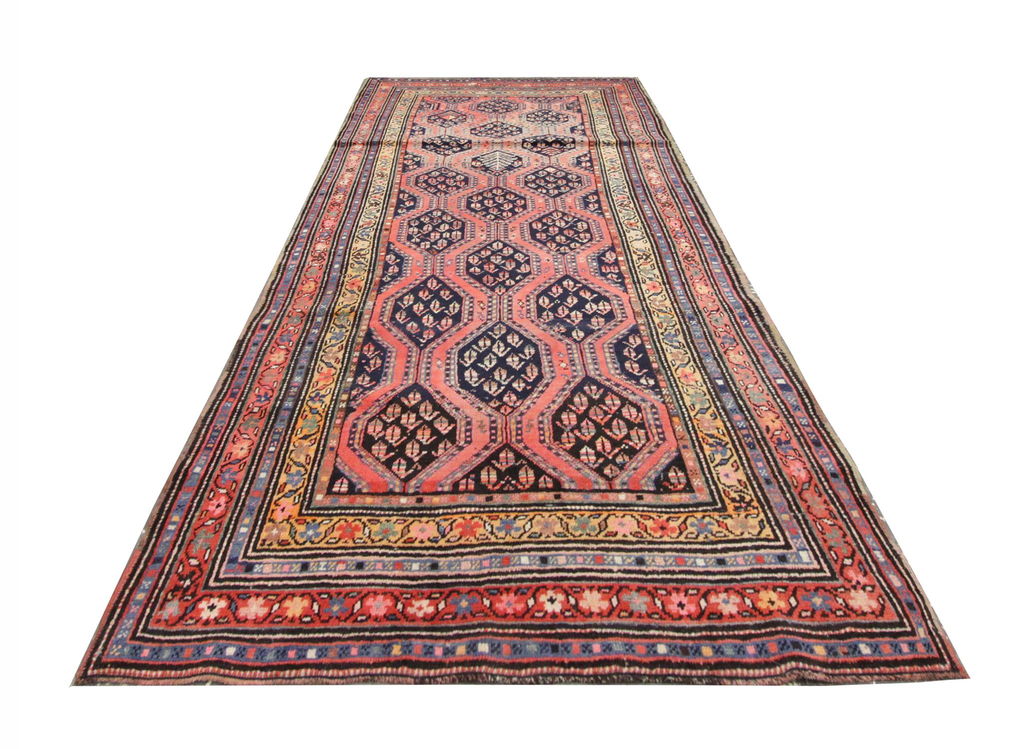 This stunningly detailed runner rug has been beautifully handwoven in many beautiful colourways. A multi-layered border or linear floral patterns in Blue, pink, and yellow frames the central design. On a background of peachy pink sits a symmetrical