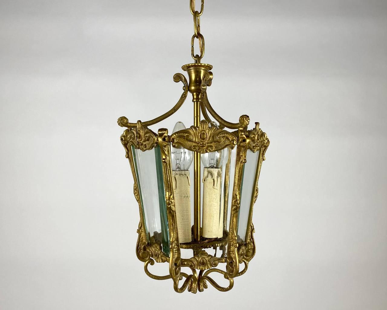 Amazing gilded bronze double light antique hall lantern, the two scrolling light fittings with circular reeded bobeche drip pans, surrounded by sectional convex tapering glass panels and held within a foliated scrolling framework with decorative