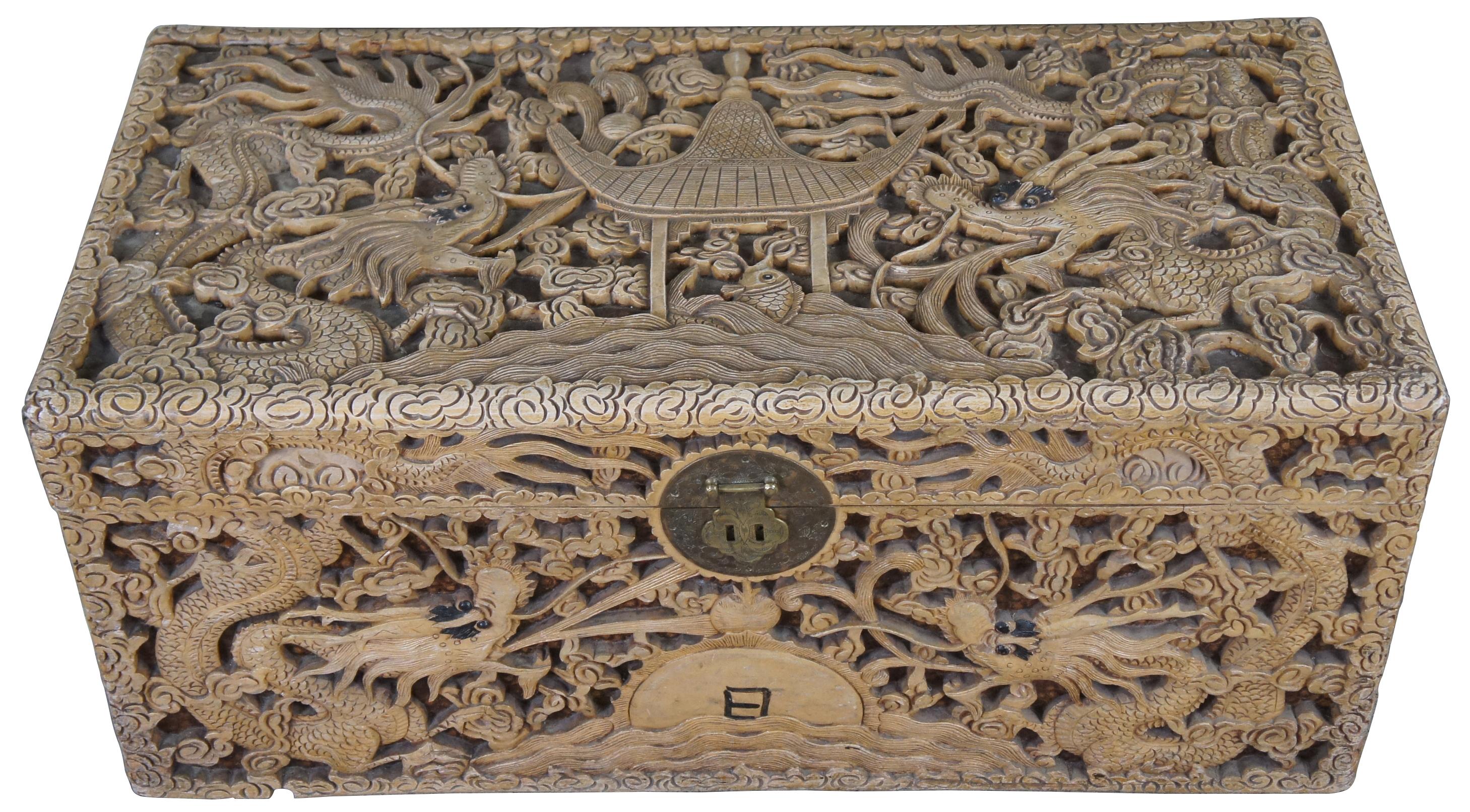 An exceptional and rare early 20th century camphor wood cehst. Profusely carved in high relief sculpting with fire breathing dragons amidst a field of clouds waterside sunset and pagoda scene with fish. Features handles, brass center plate and paper