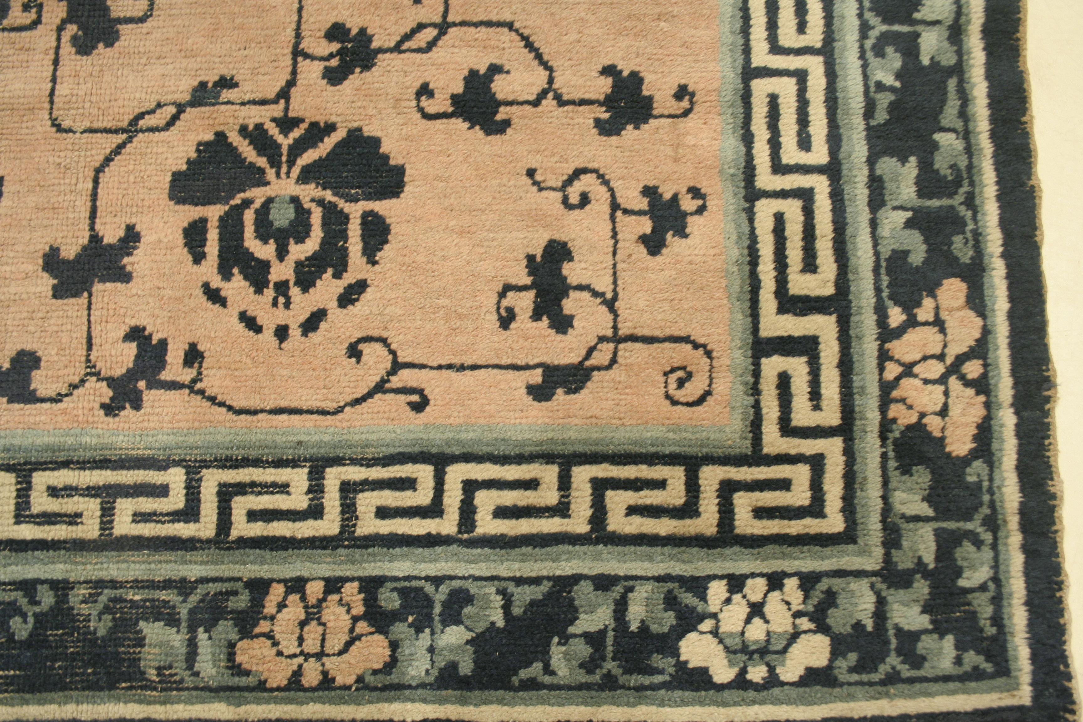 This rare Ningxia rug features a blush pink background decorated by a directional pattern of large blue lotus flowers, symbols of long life, connected by a thin leafy vinery. The blue border is adorned with ivory and rose peonies, and the inner