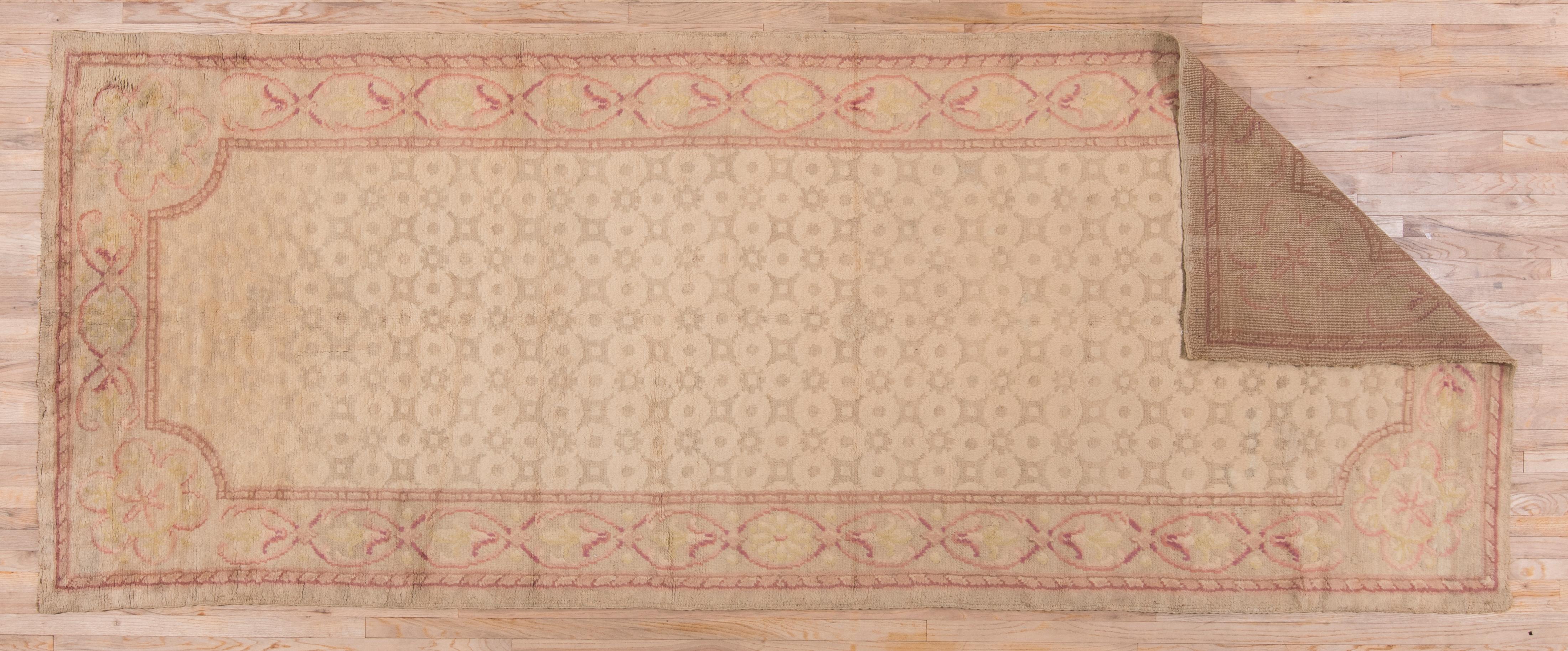 This thick, heavy European carpet in the Art Deco style features a sandy beige field with a small octagon and square repeating pattern and roundly beveled corners. The tonally end suite border shows ellipses with flowers or stars. Light palette with